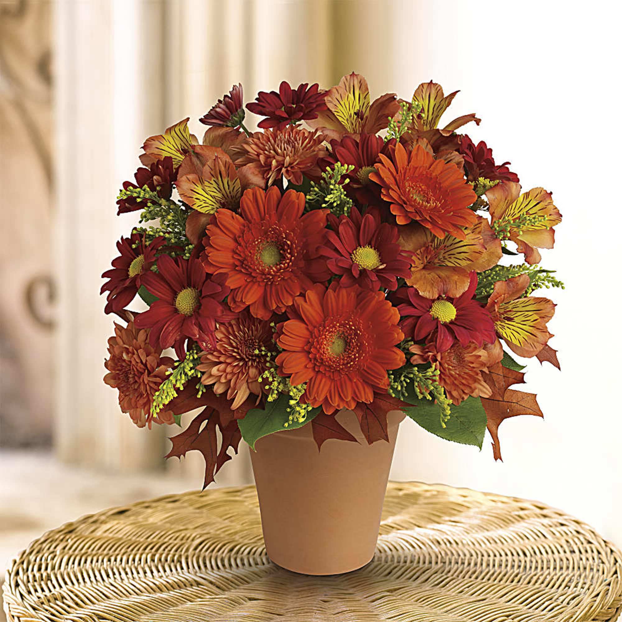 Orange and red mixed flower arrangement in a tan pot