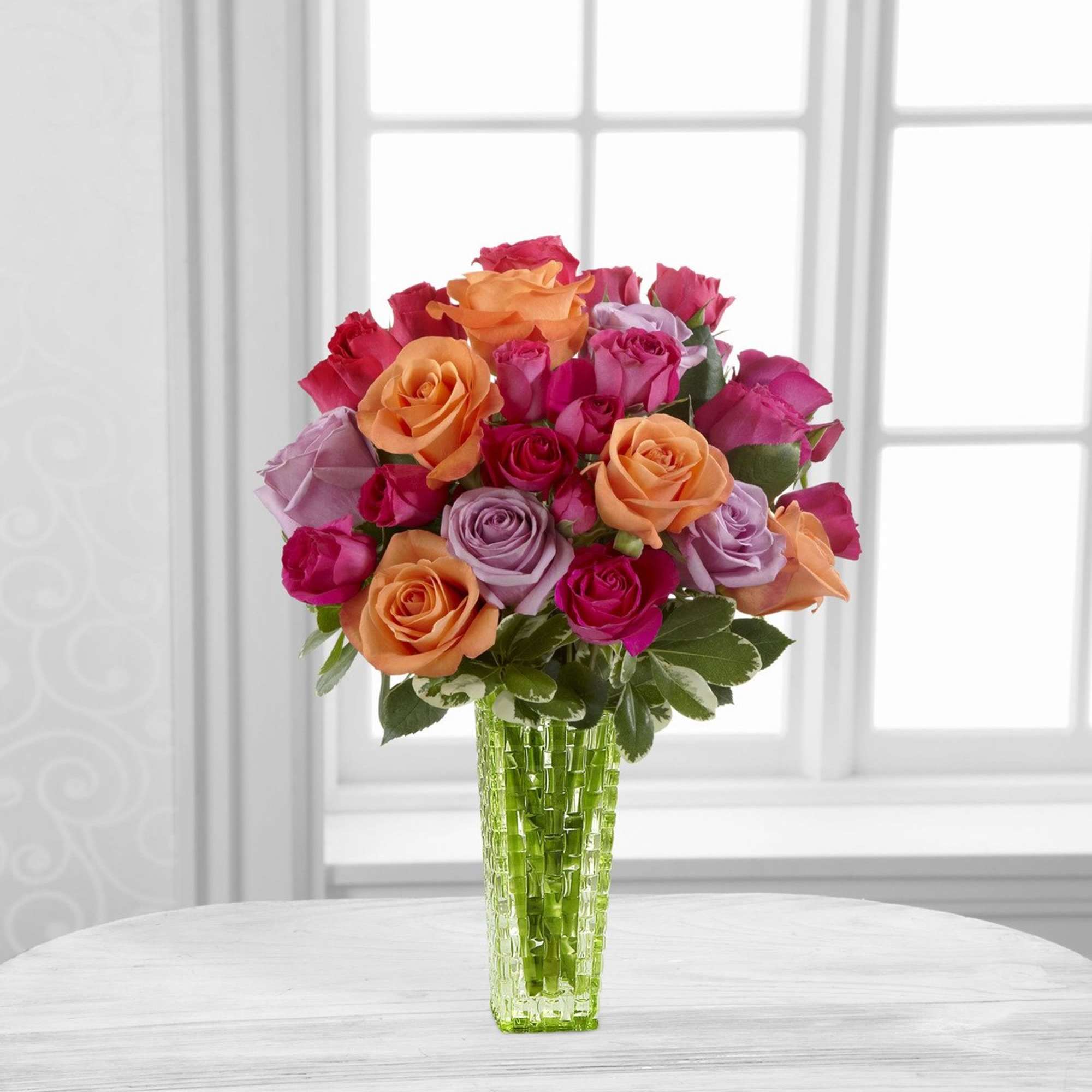 Bouquet of pink, orange, and lavender roses in a green glass vase
