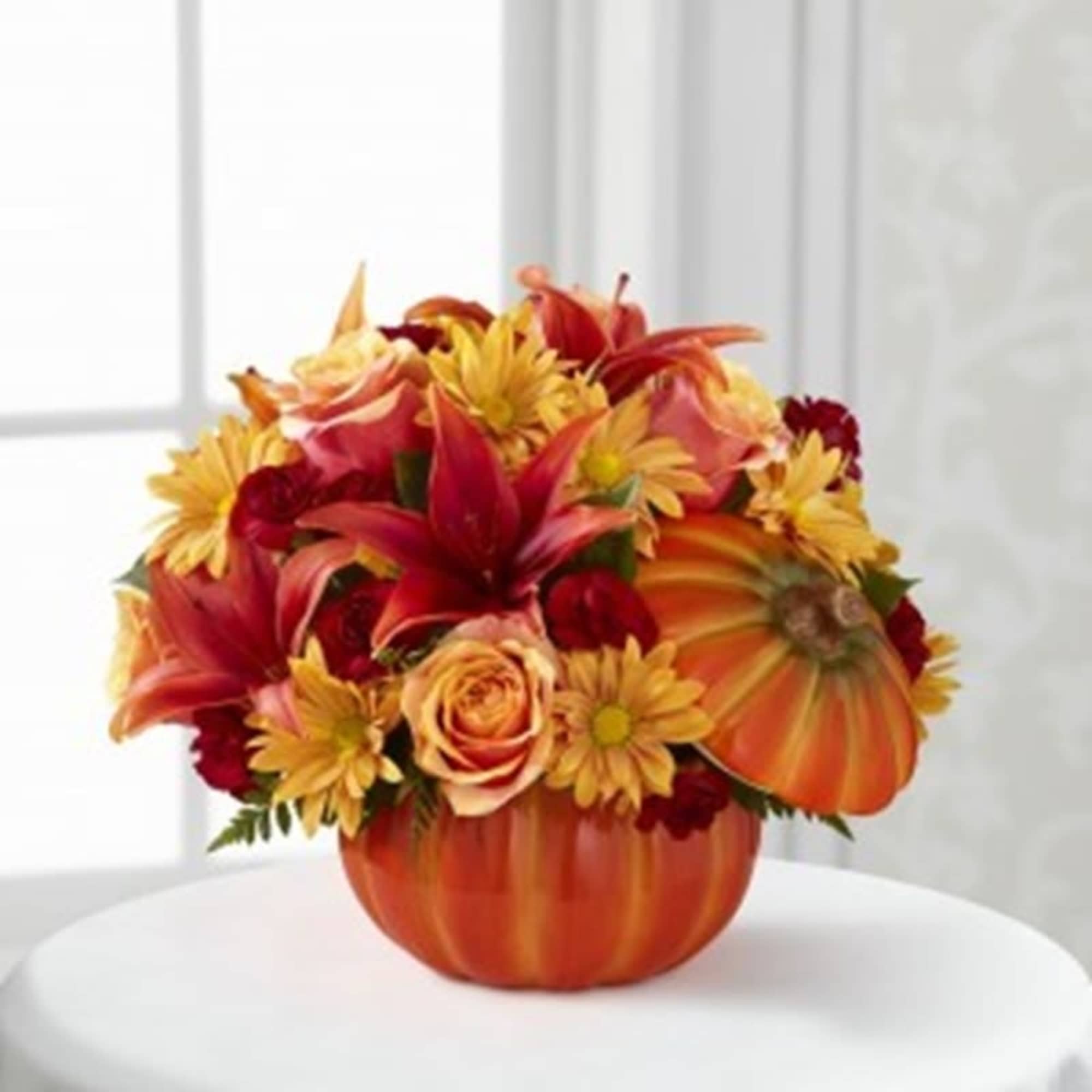 Orange pumpkin vase filled with red and yellow flowers