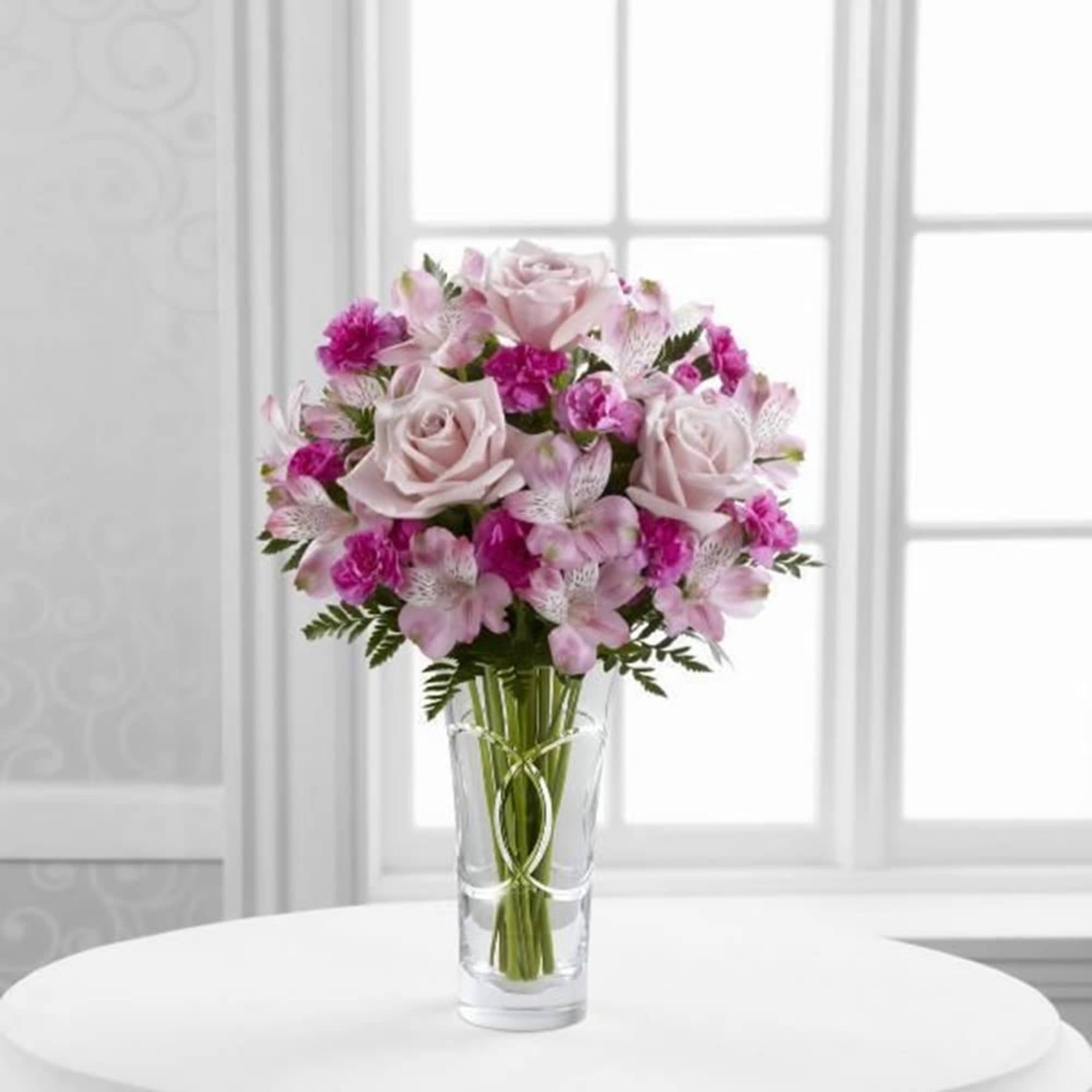 Pink and white bouquet of roses and small filler flowers in a clear glass vase