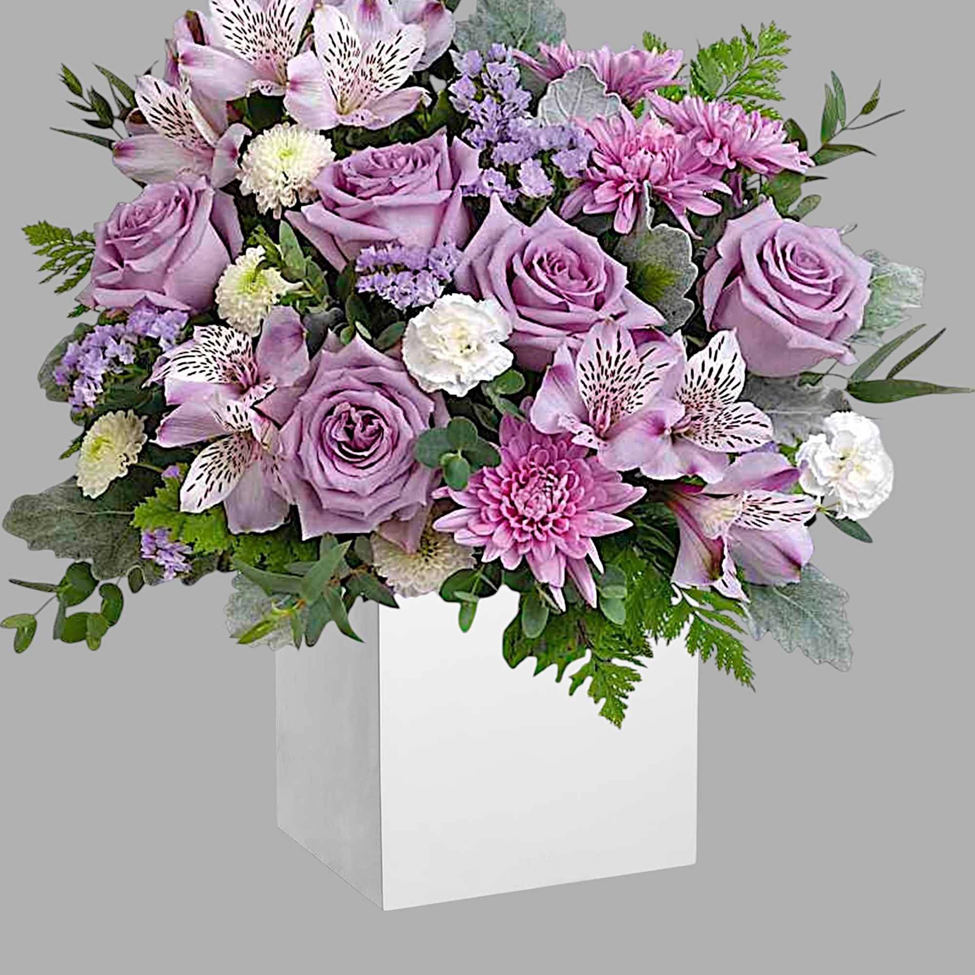 Lavender roses and mixed blooms arranged in a white box