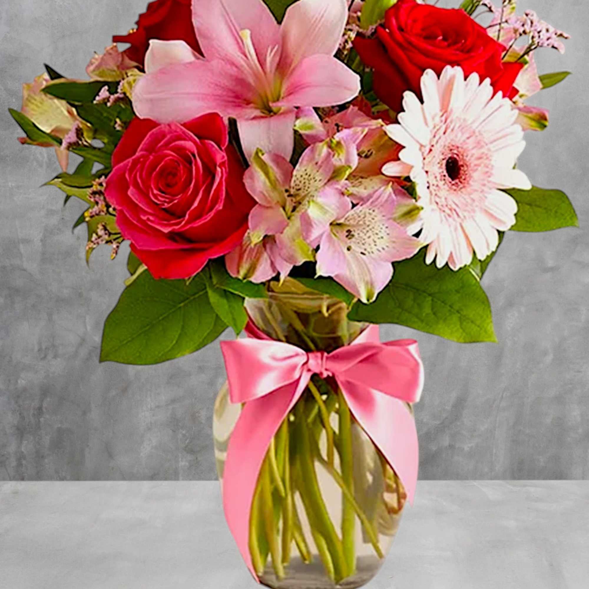 Bouquet of pink lilies, red roses, and a white gerbera daisy in a glass vase