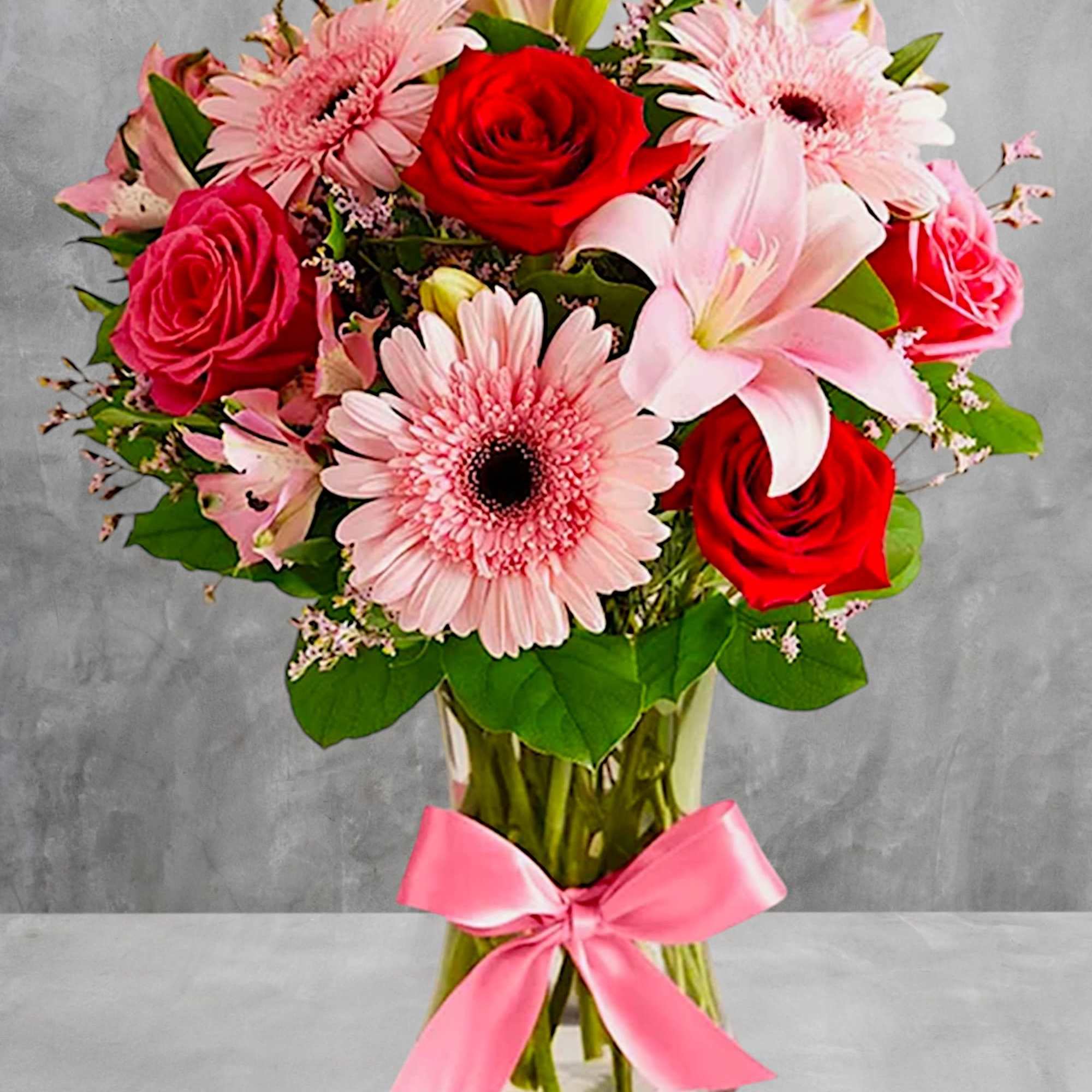 Pink and red flower bouquet in a glass vase with a pink ribbon