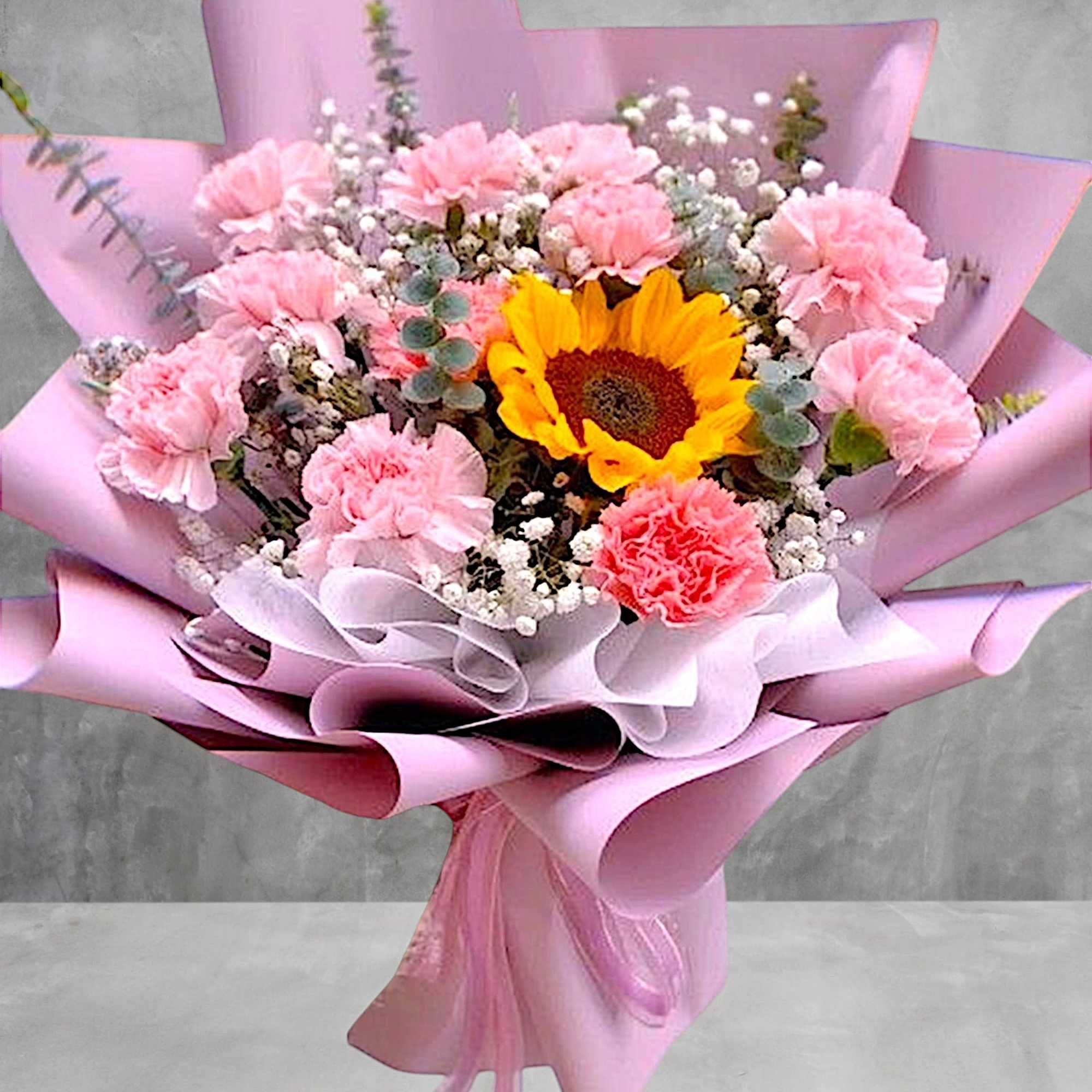 Pink bouquet with a sunflower, carnations, and baby's breath wrapped in pink paper