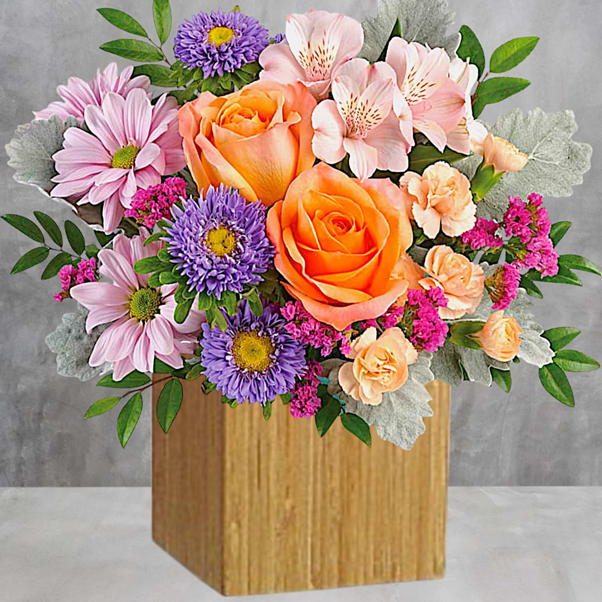 Mixed bouquet with orange roses, pink daisies, and purple flowers in a wooden box