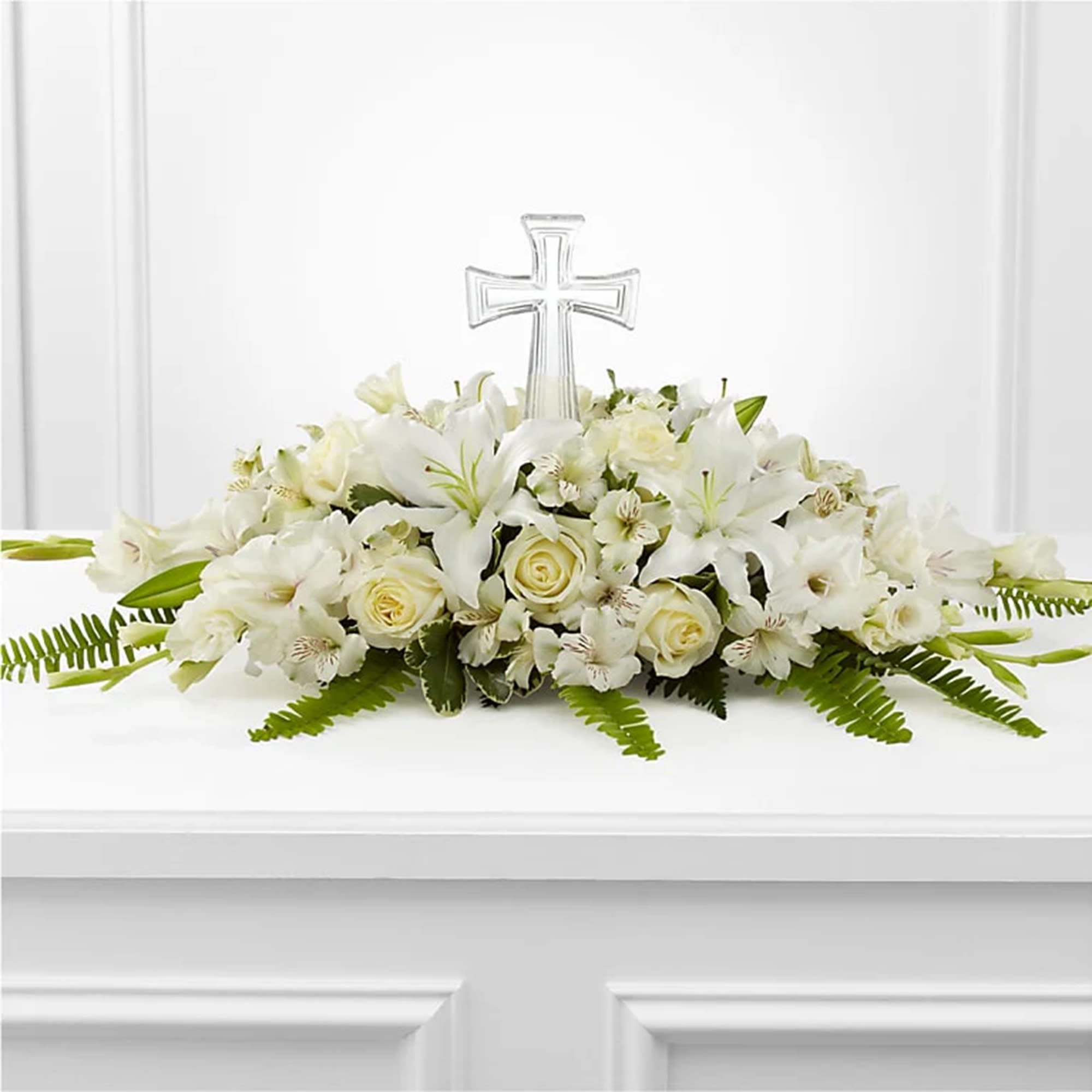 White funeral spray with roses and lilies topped by a clear cross