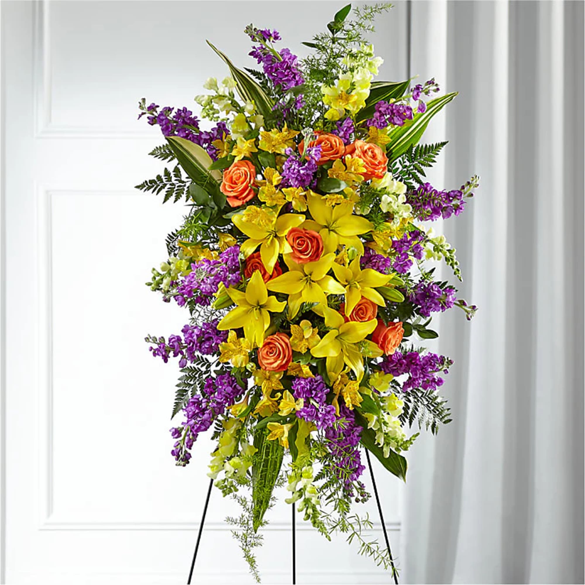 Tall standing floral spray with yellow lilies, orange roses, and purple flowers