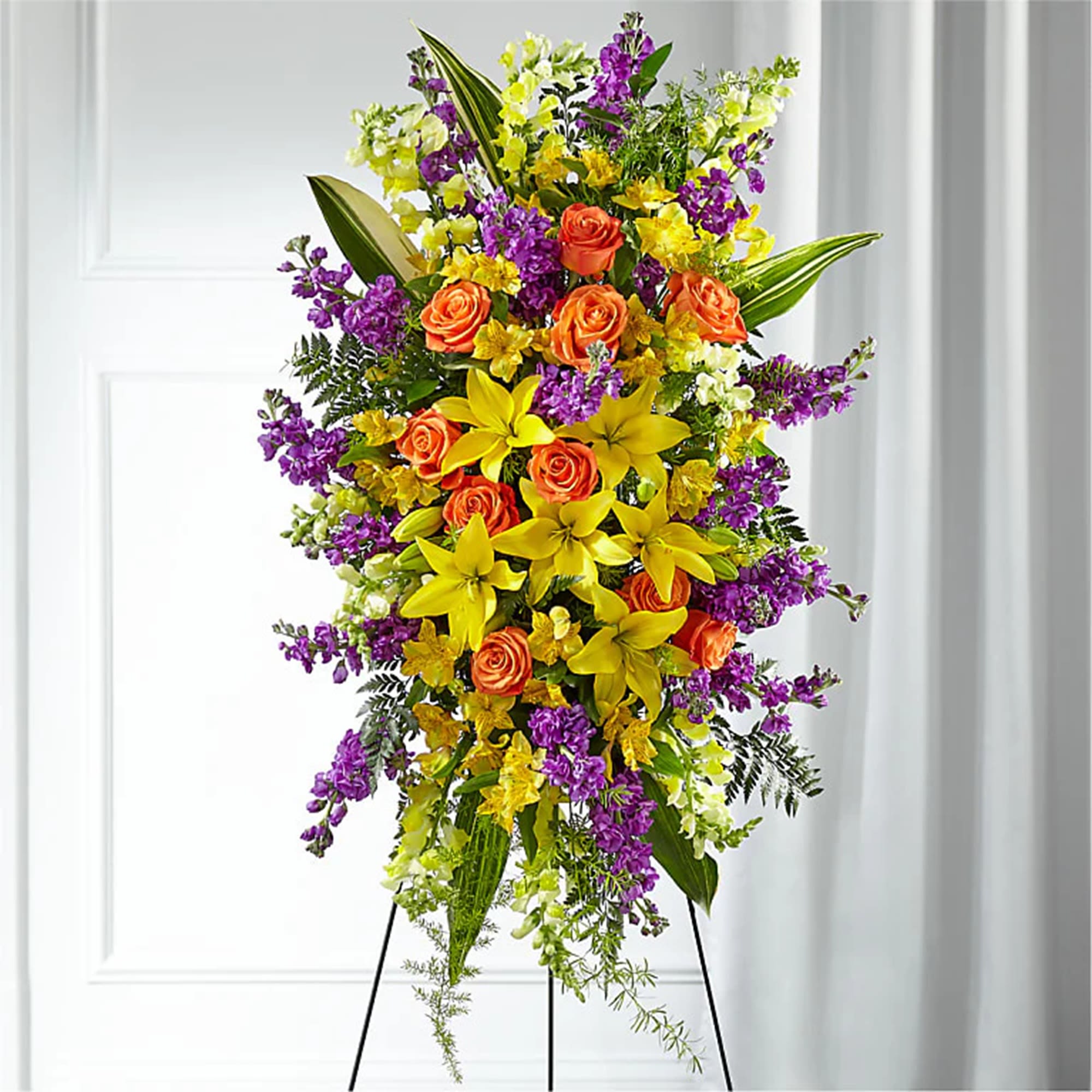 Tall standing floral spray with orange roses, yellow lilies, and purple flowers