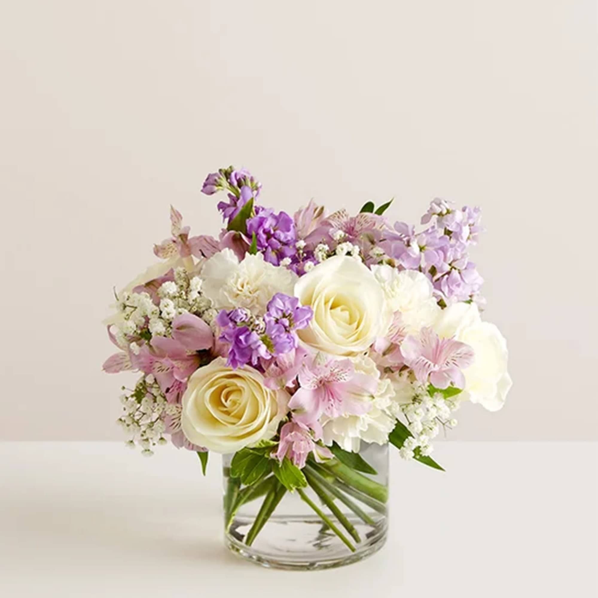 Pastel bouquet of roses and purple flowers in a clear glass vase