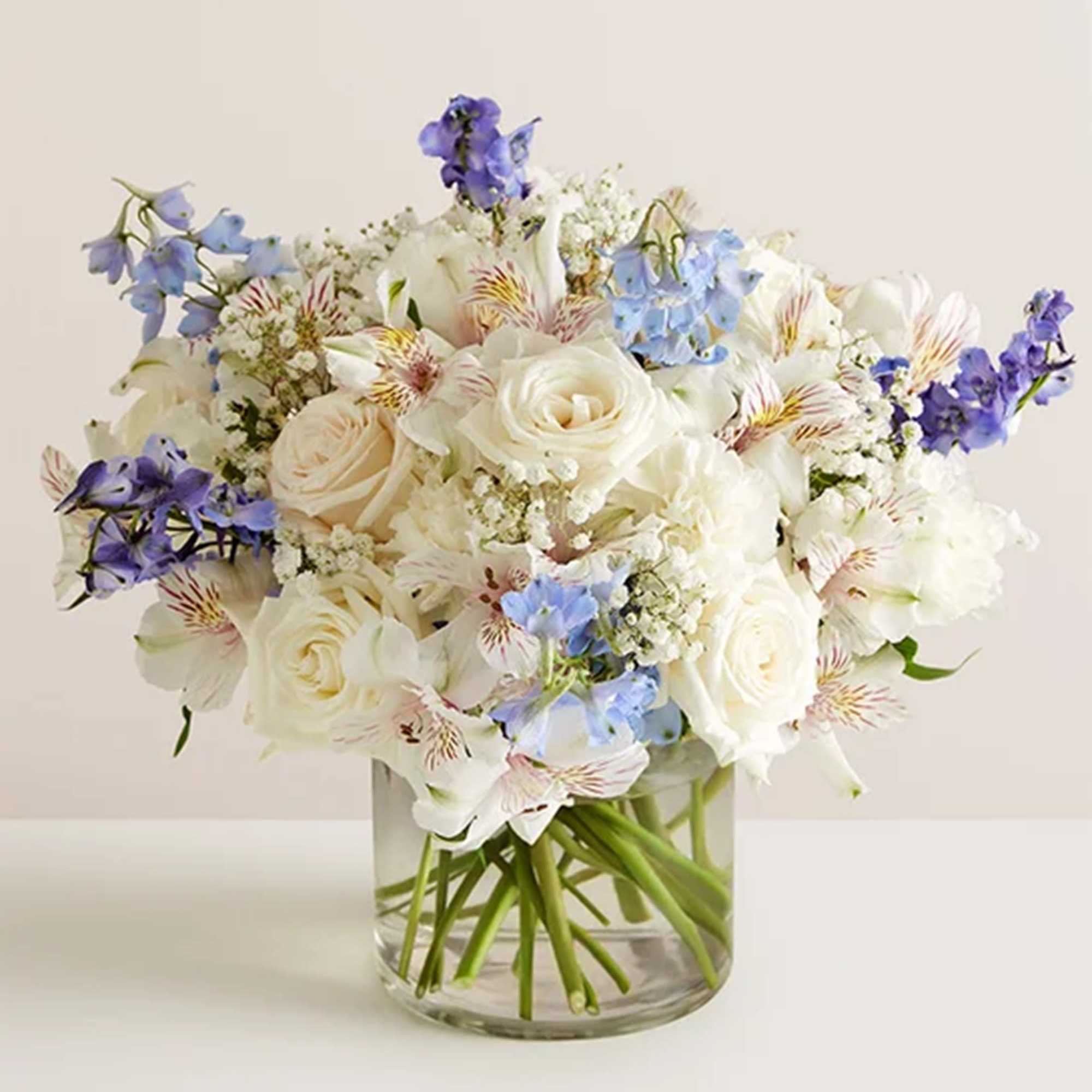 White roses and blue flowers in a clear glass vase