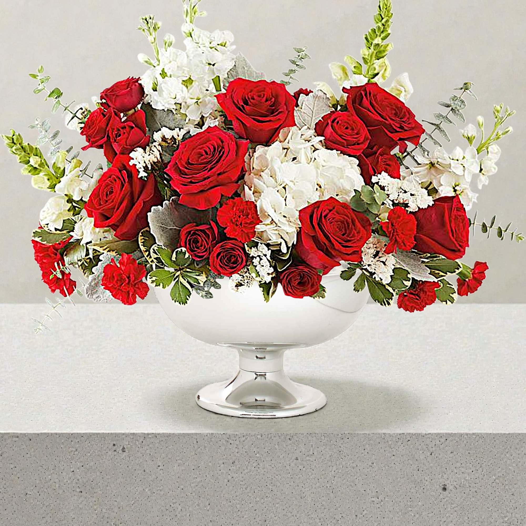 Red roses and white flowers arranged in a white pedestal bowl
