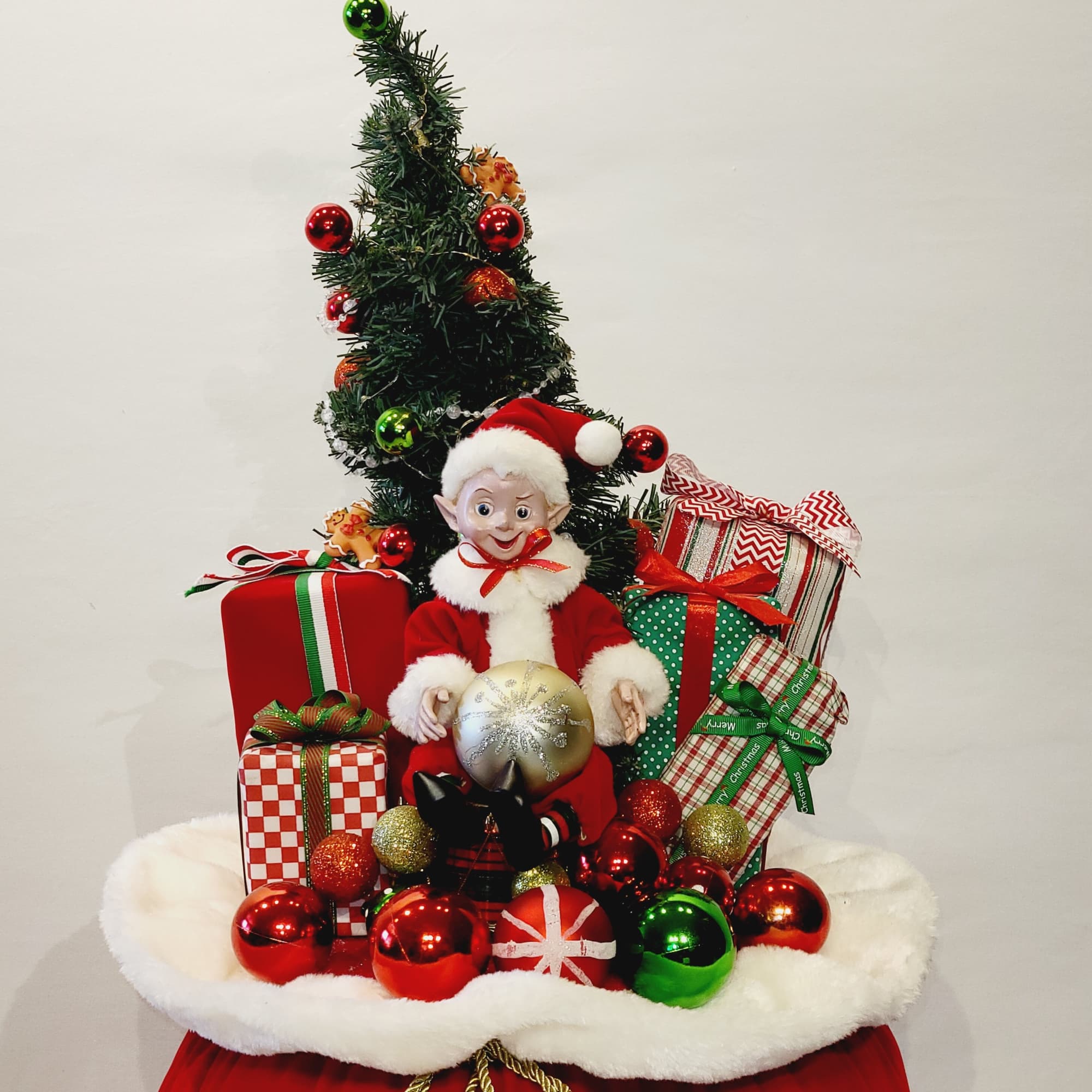 Christmas elf figurine with wrapped gifts and ornaments on a white fur base