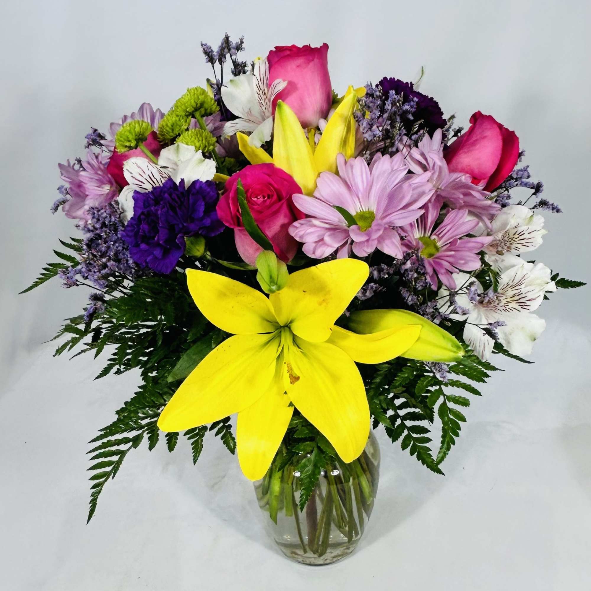 Mixed bouquet of yellow lilies, pink roses, and assorted blooms in a clear glass vase