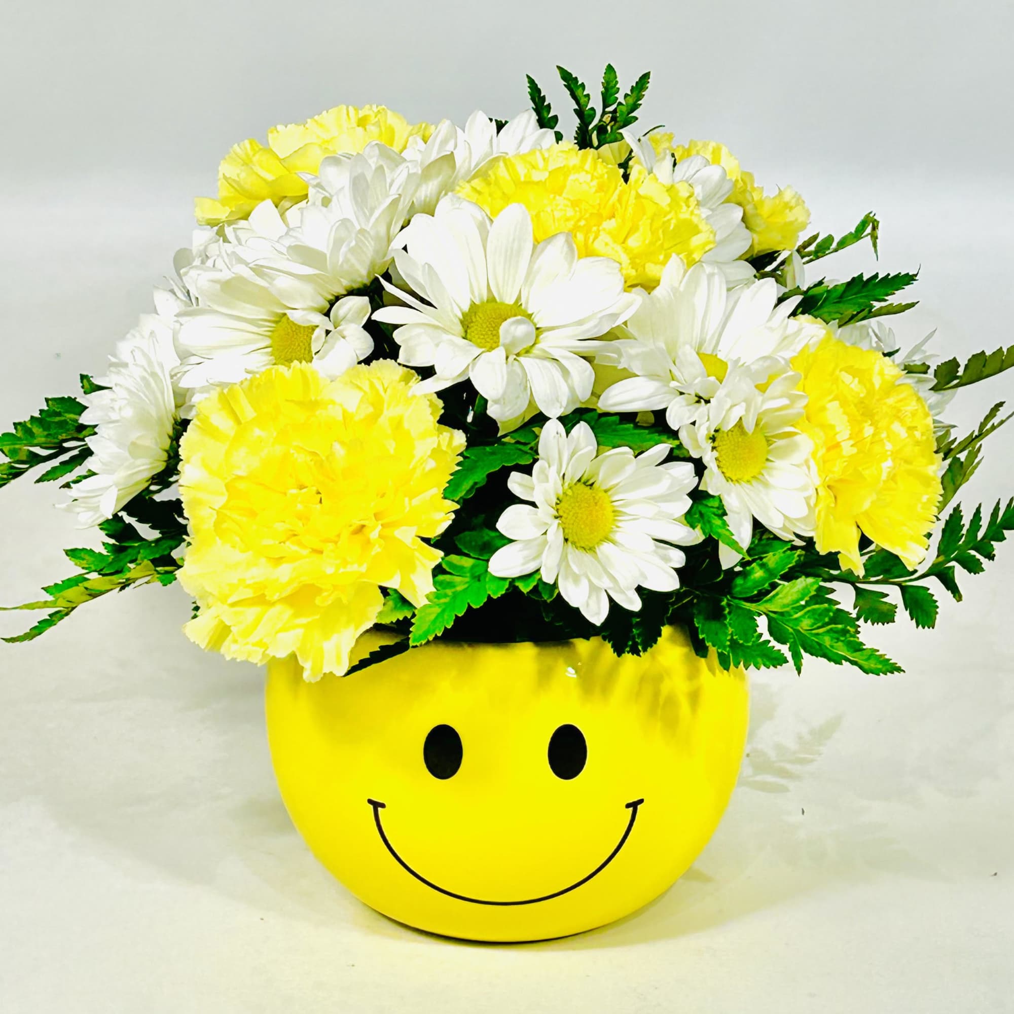 Yellow and white daisy bouquet in a smiley-face pot