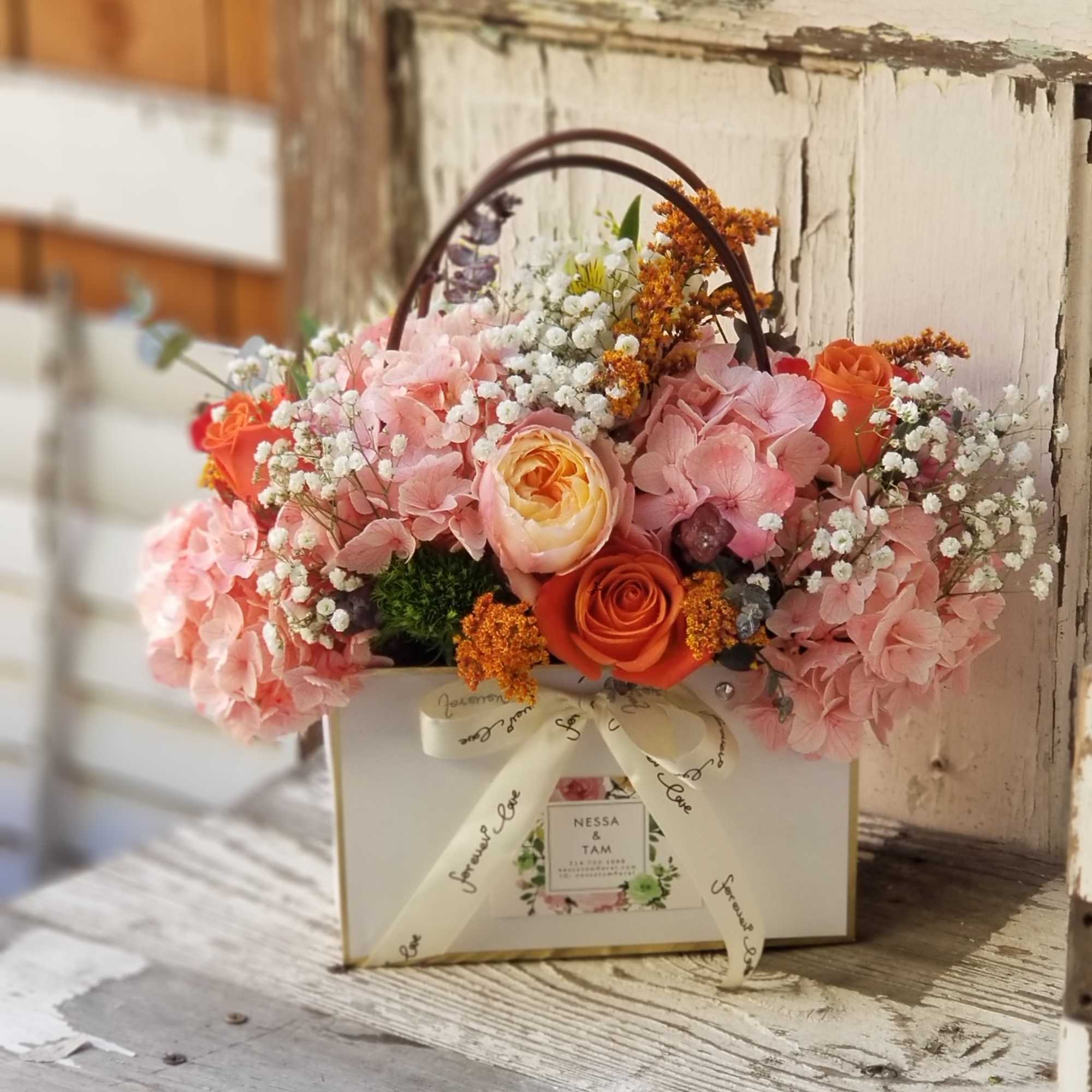 Pink and orange flower arrangement in a white gift box with ribbon handle