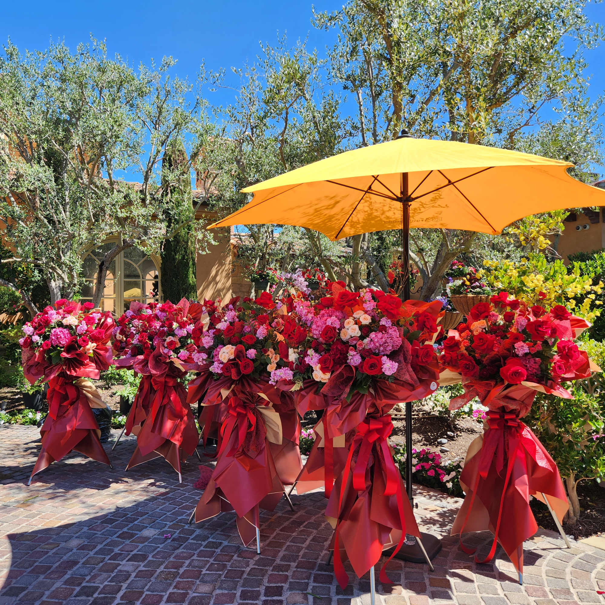 Large outdoor display of red and pink floral arrangements under a yellow umbrella