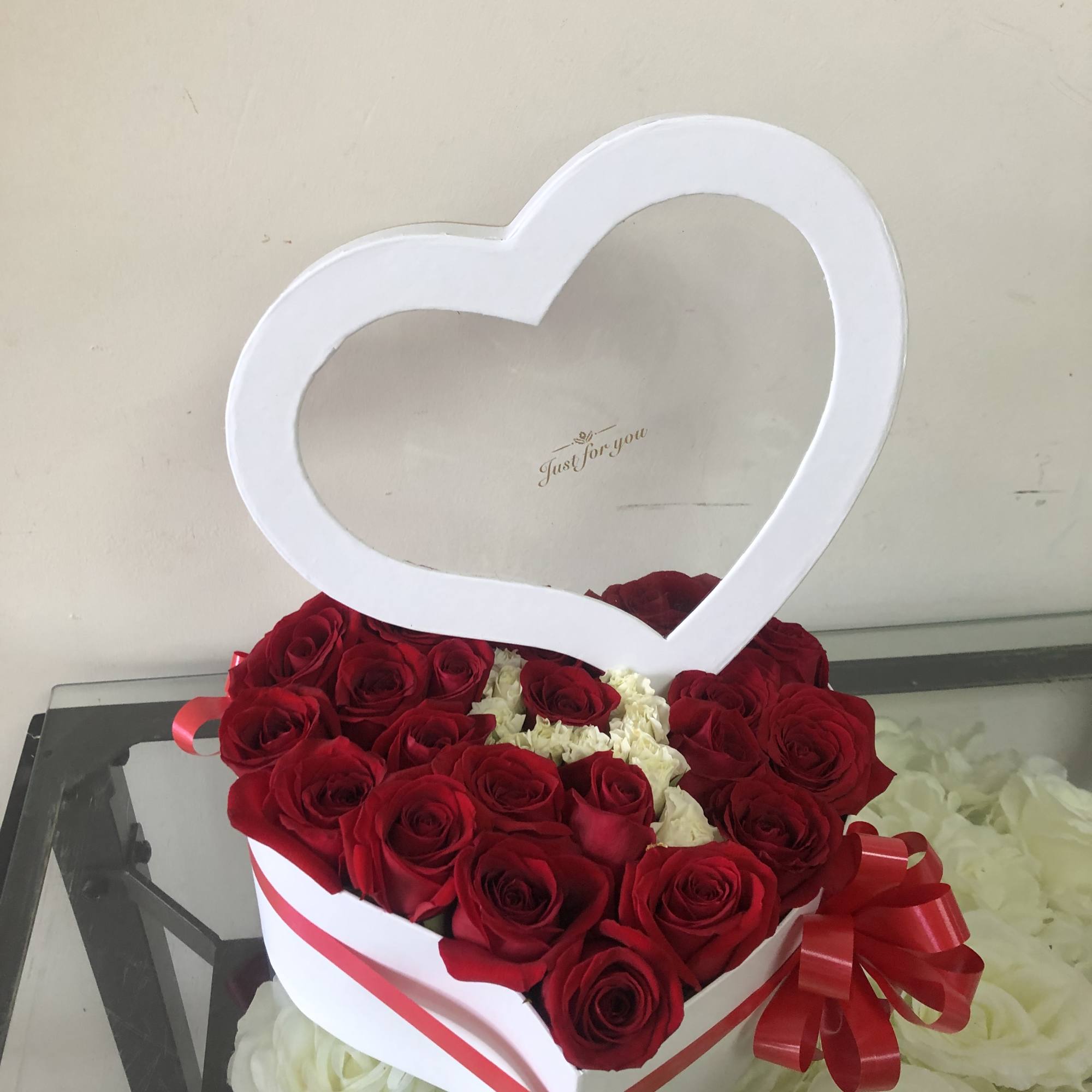 Heart-shaped box of red roses with a white heart topper and red ribbon