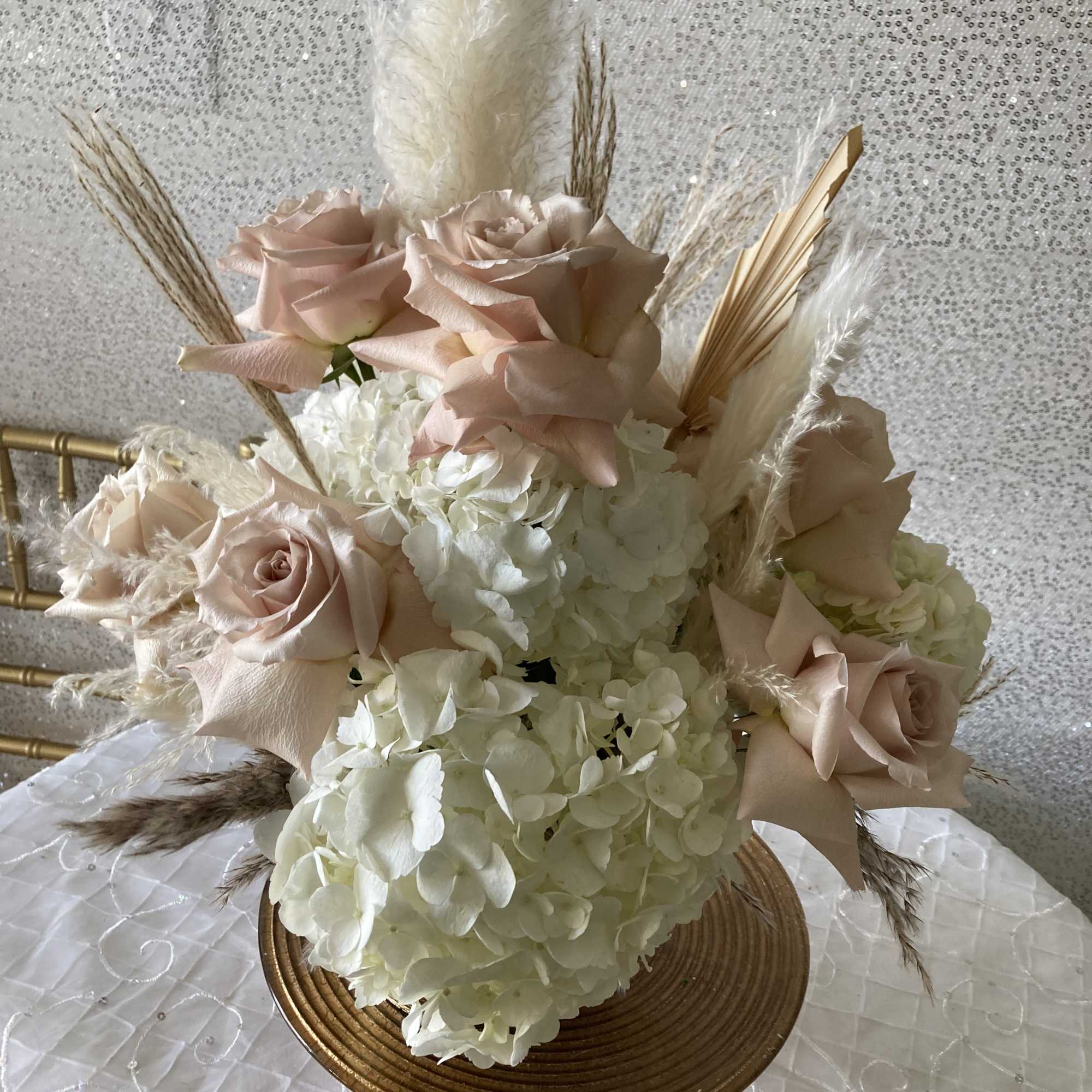Blush roses and white hydrangeas in a gold vase with dried grasses