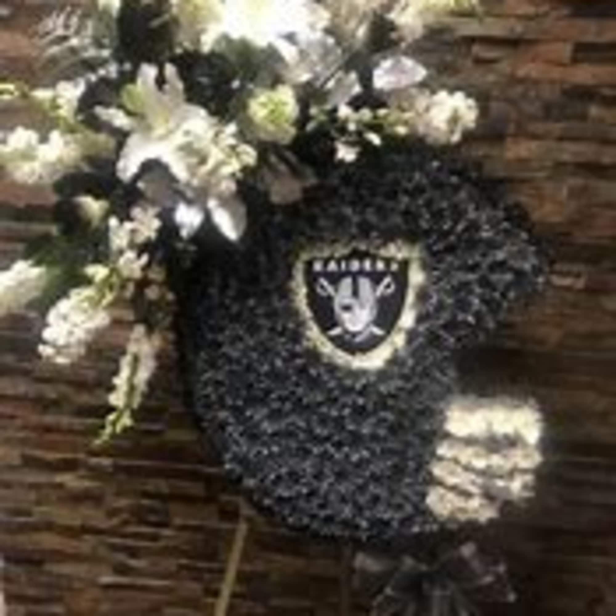 Black floral wreath with white flowers and a Raiders emblem