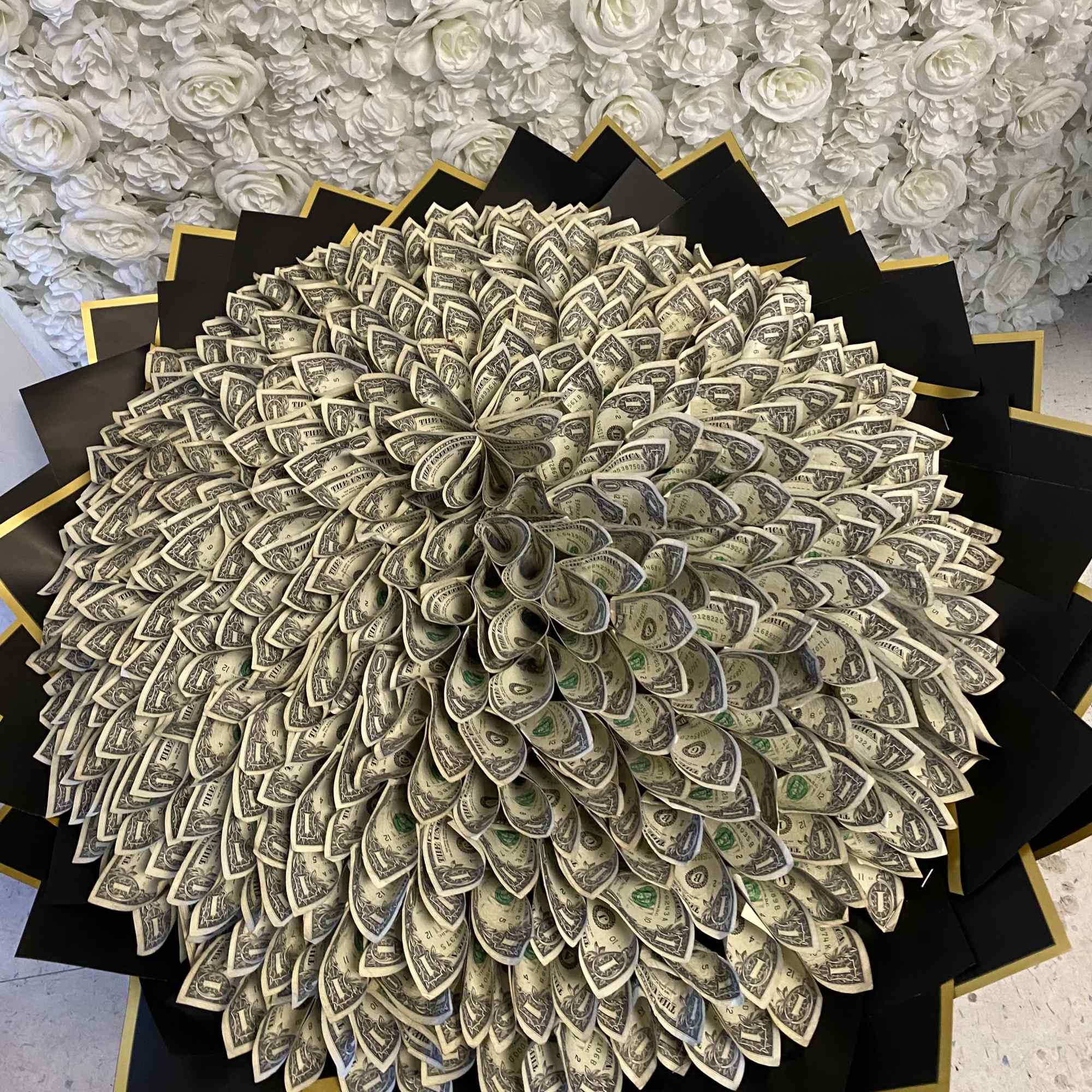 Large bouquet made of folded dollar bills against a white floral backdrop