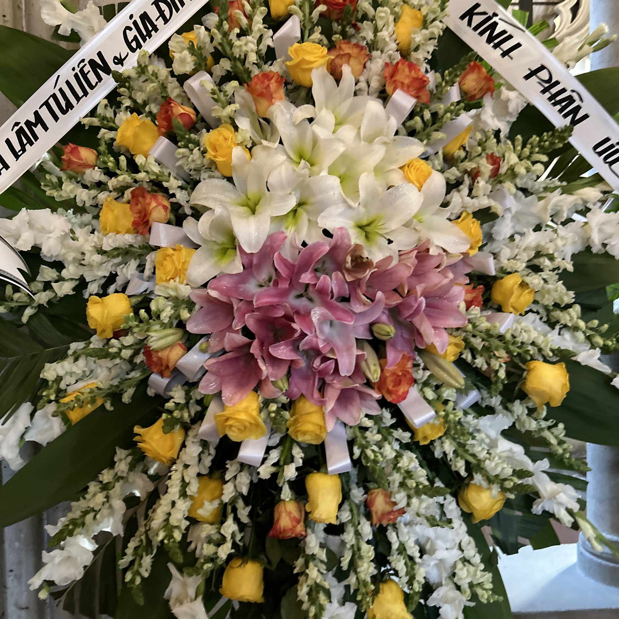 Large funeral wreath with white lilies, pink orchids, and yellow roses