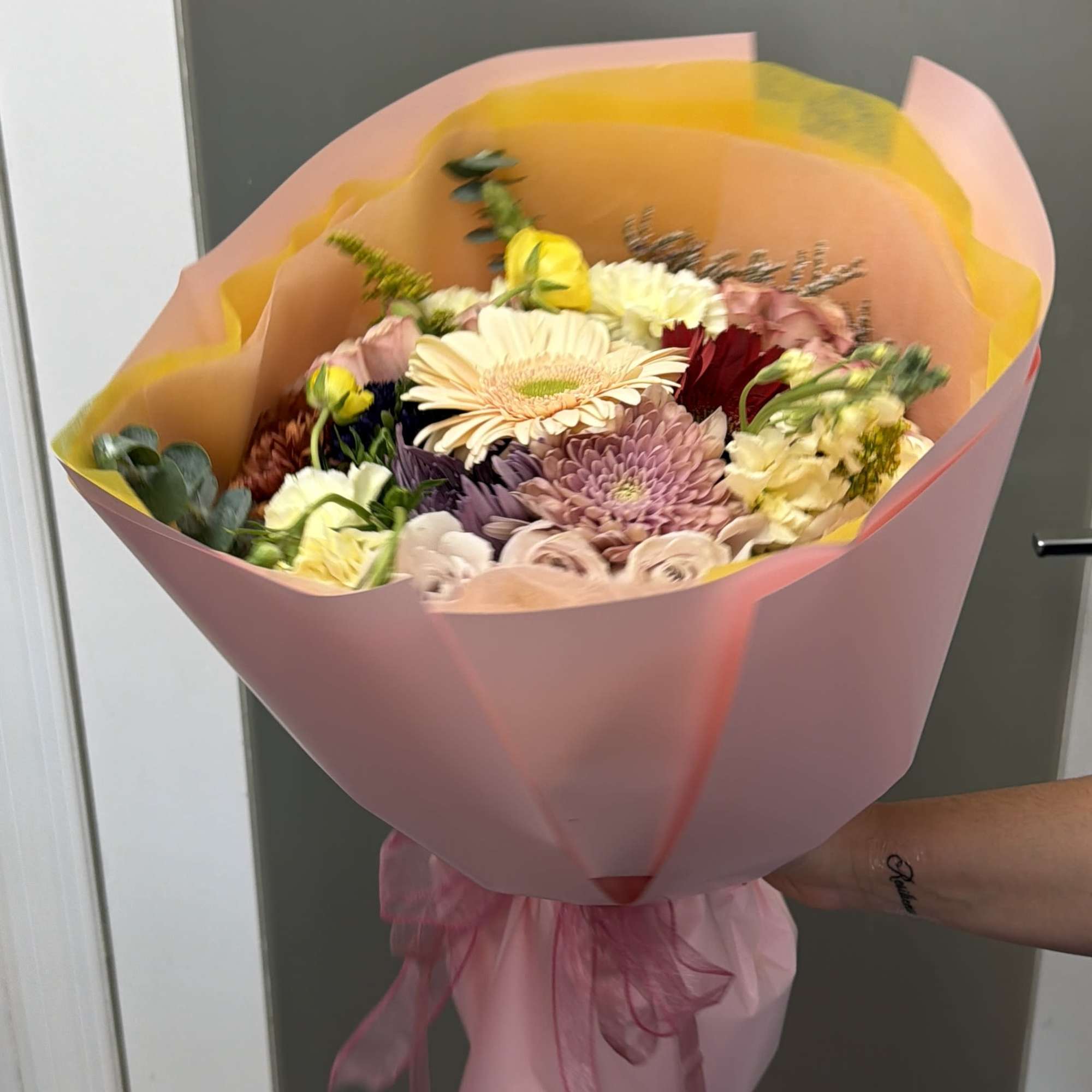 Hand-tied bouquet of mixed pastel flowers wrapped in pink paper