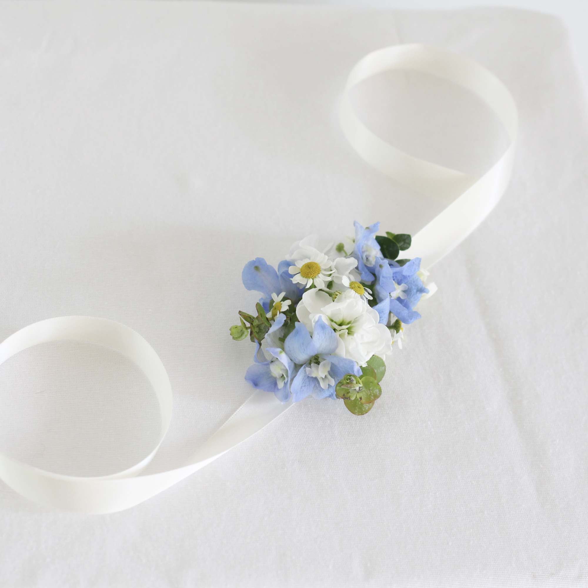 Small blue and white floral wrist corsage with ribbon