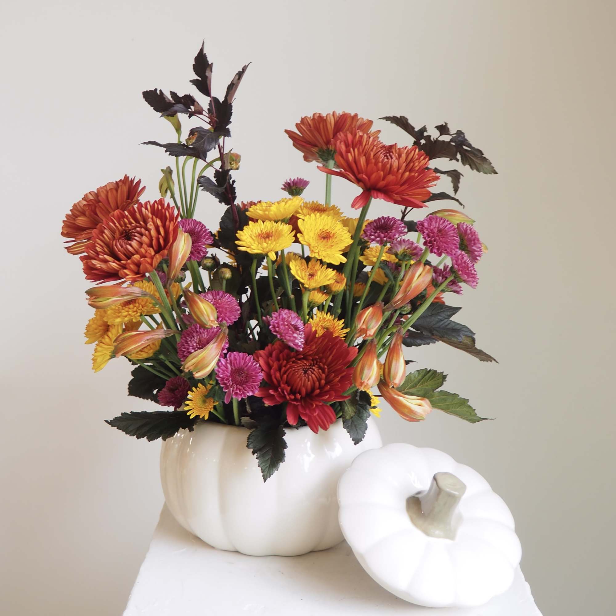 Mixed bouquet of orange, yellow, and pink flowers in a white pumpkin vase