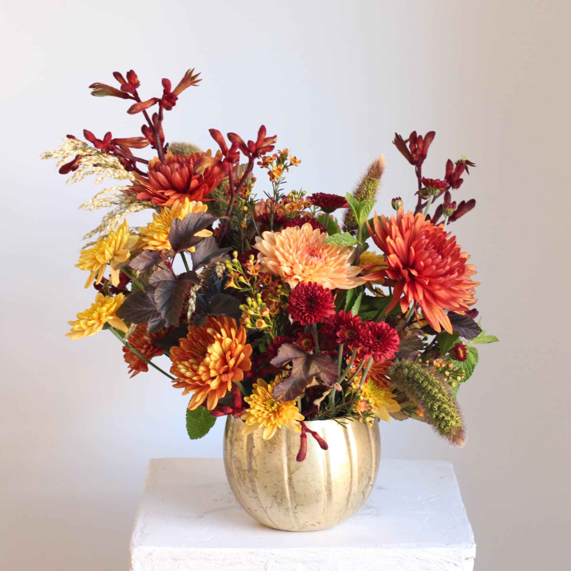 Autumn bouquet of orange, yellow, and red flowers in a gold vase