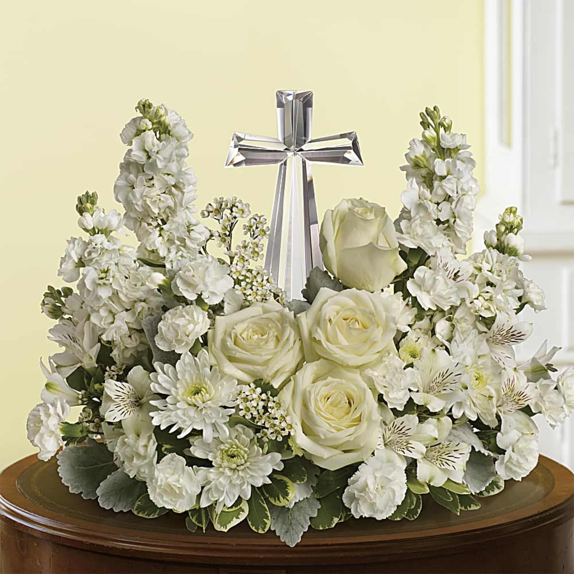 White sympathy flower arrangement with roses and mums surrounding a crystal cross on a table