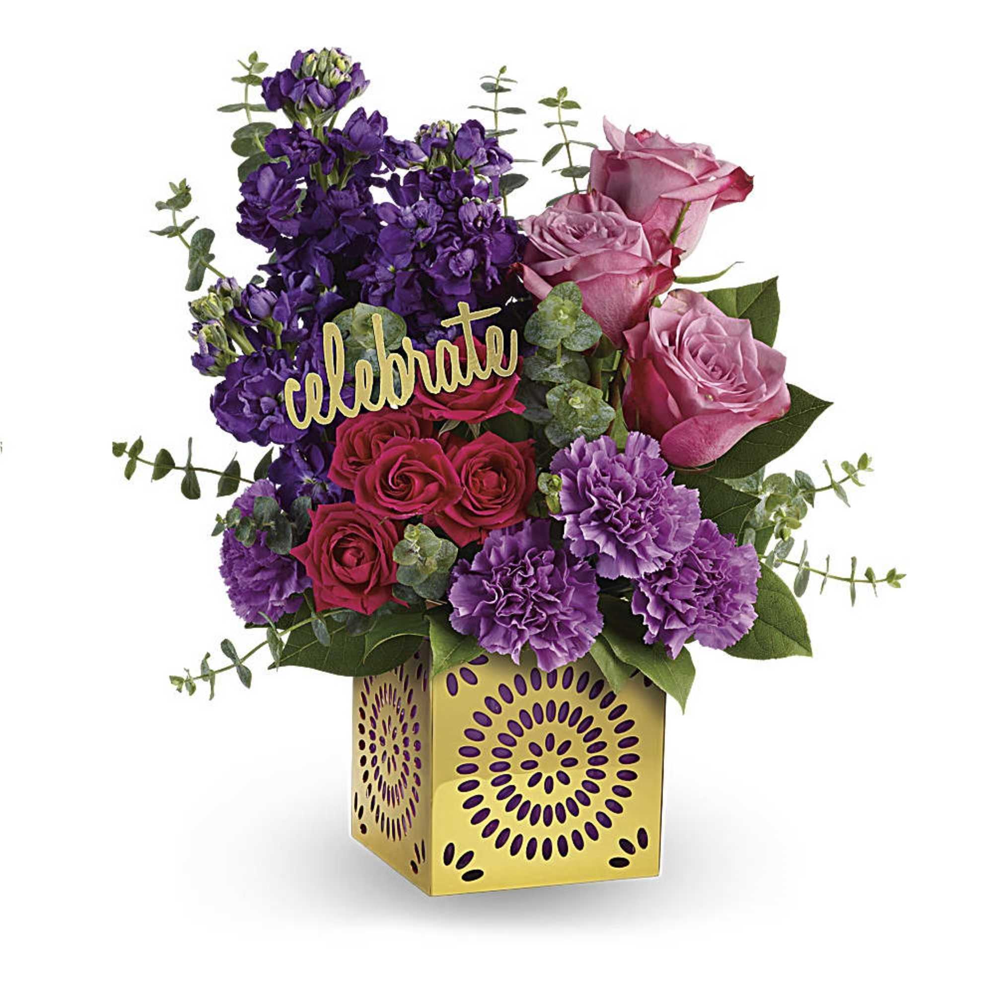Bright arrangement of pink roses, red spray roses, and purple stock in a gold cube vase with a celebrate sign