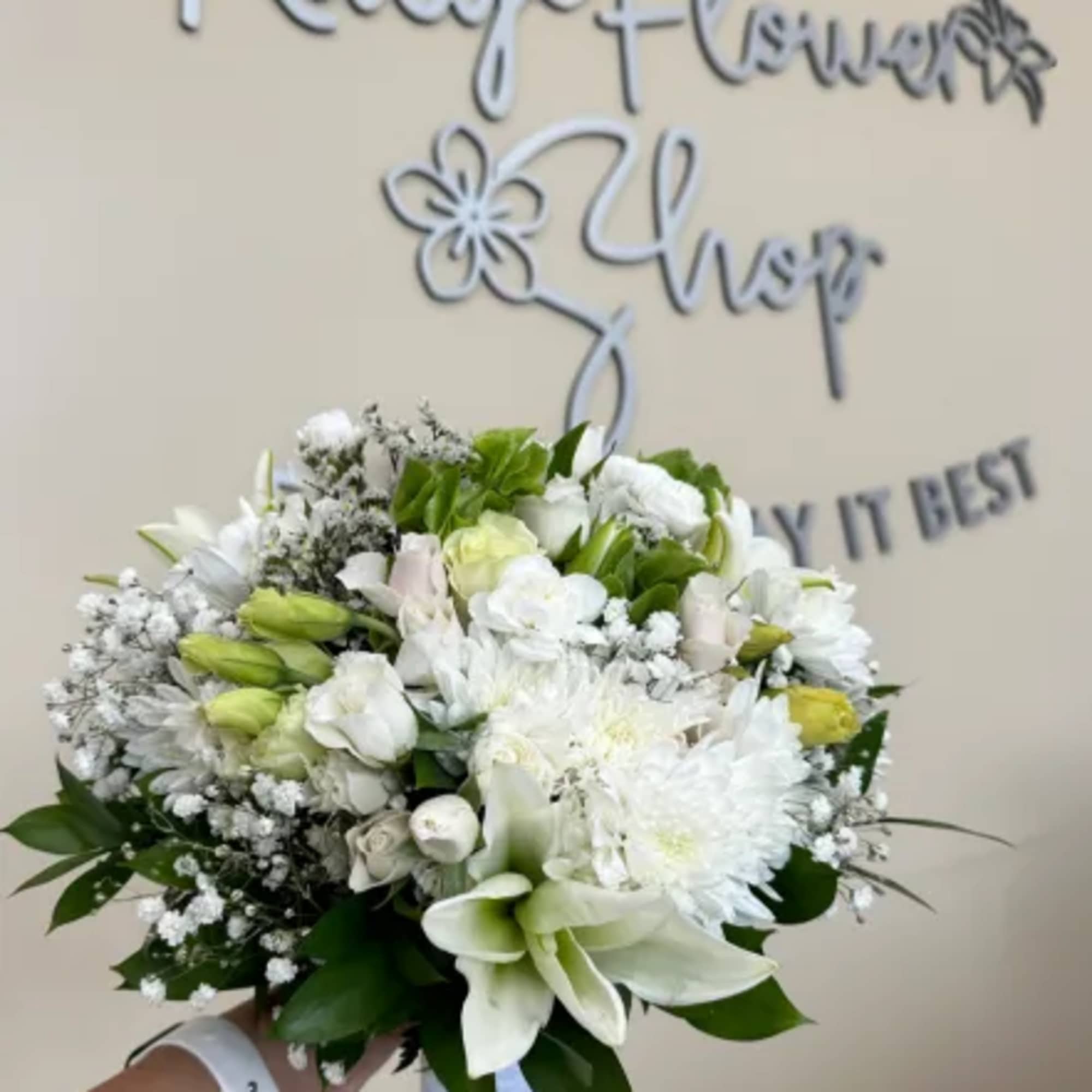Hand-tied bouquet of white lilies, roses, and chrysanthemums with small white filler flowers.