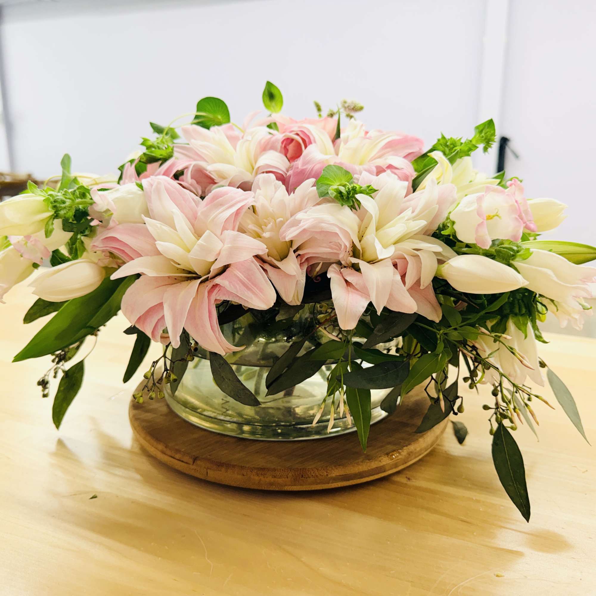Low glass bowl of pink and white lilies with greenery