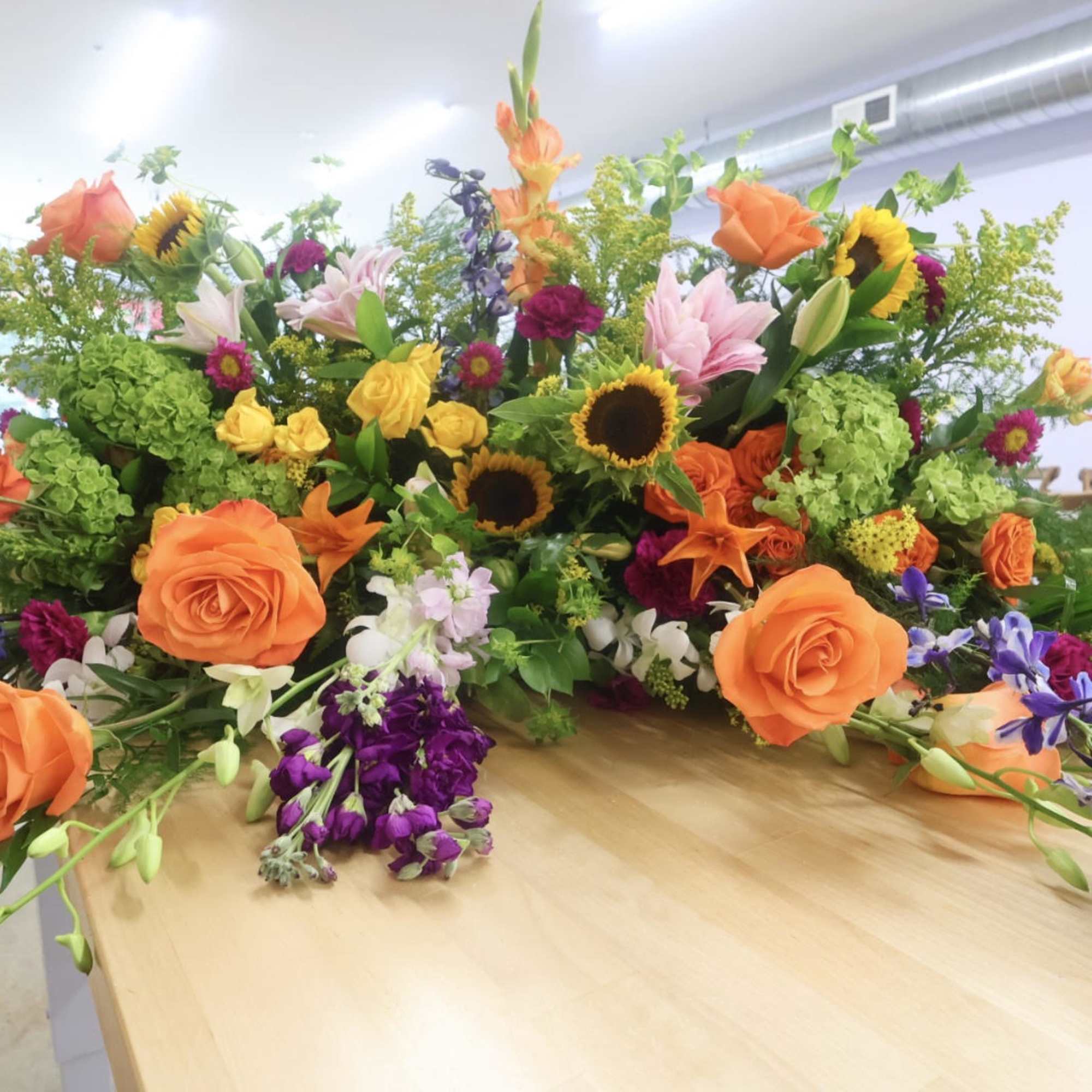 Large mixed floral arrangement with orange roses, sunflowers, and lilies on a table