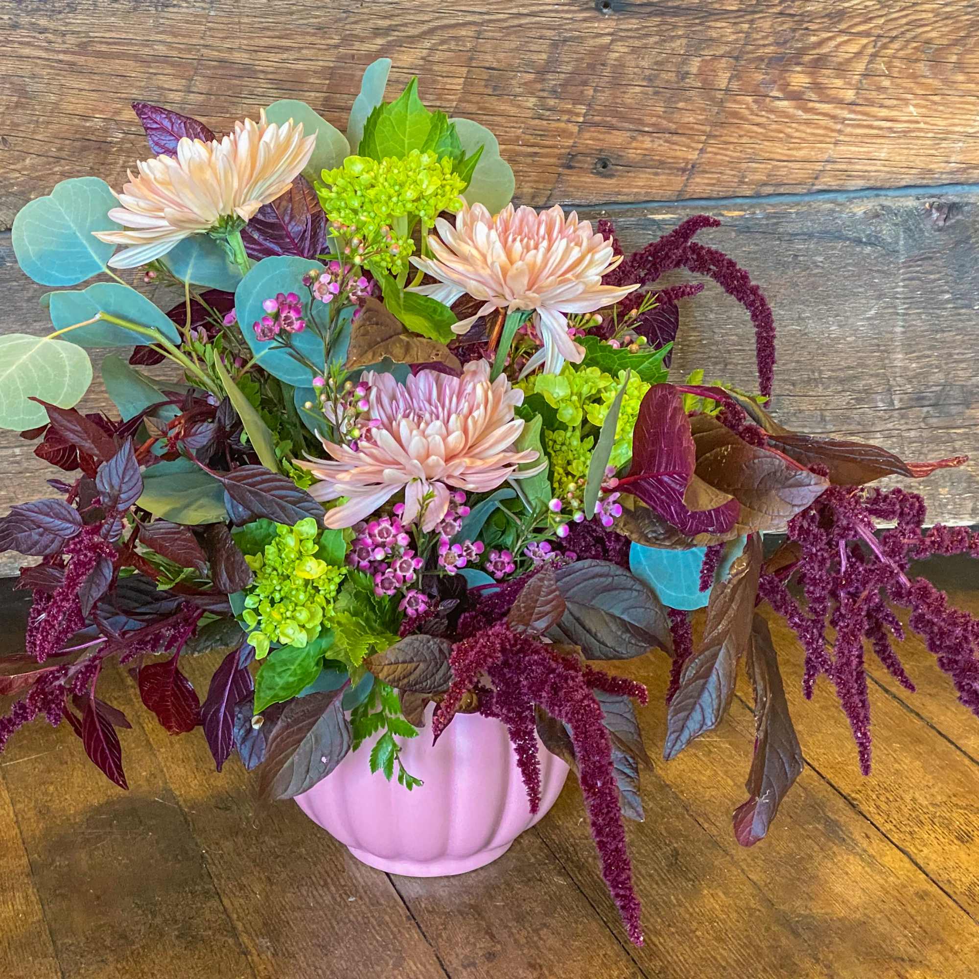 Pink chrysanthemums in a pink vase with burgundy and green foliage