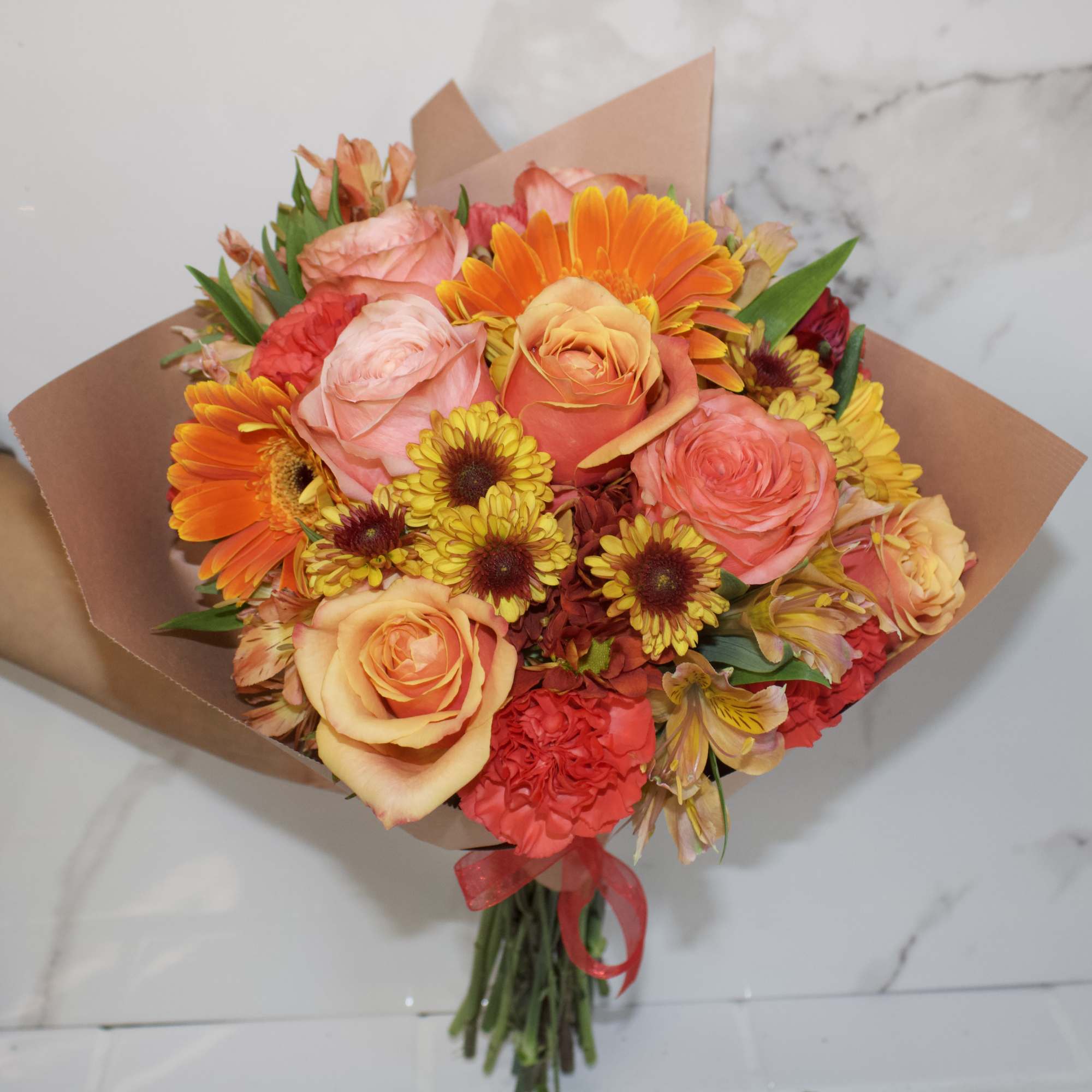 Hand-tied bouquet of orange, pink, and yellow flowers wrapped in brown paper