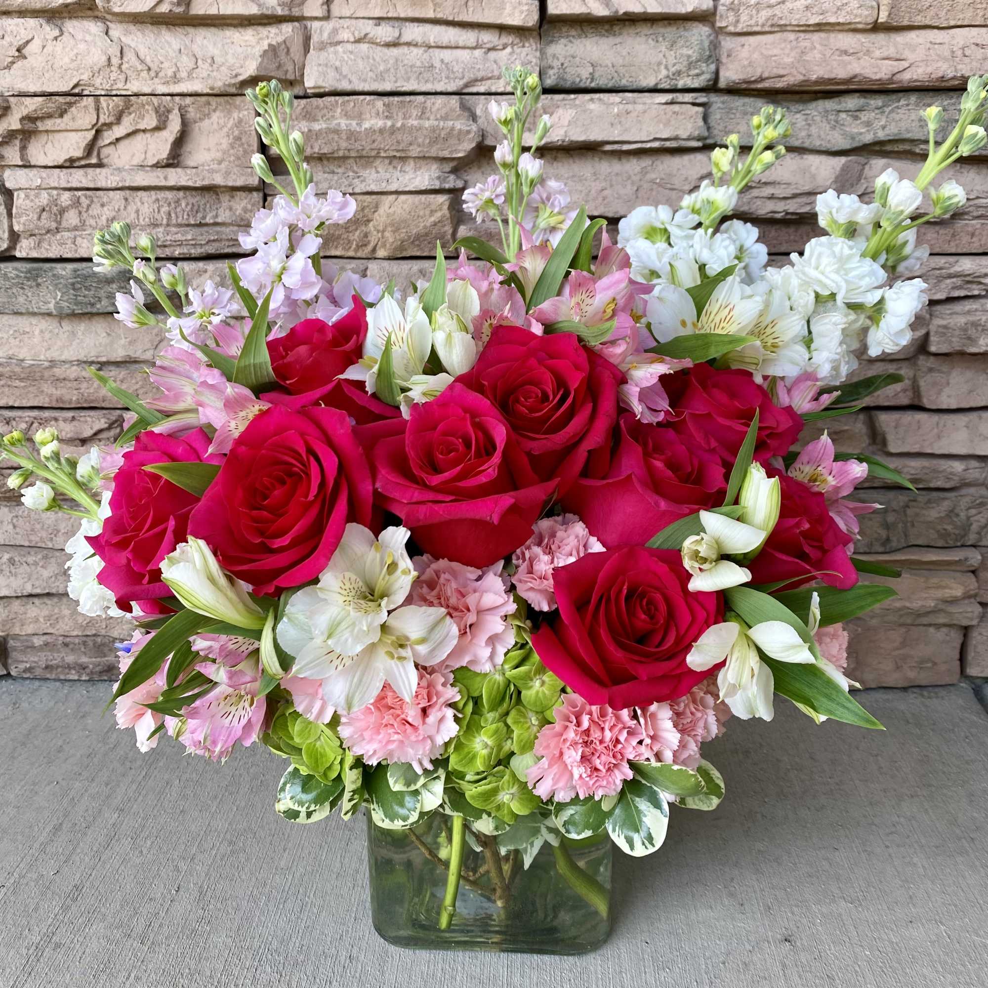 Bouquet of red roses, pink carnations, and white alstroemeria in a glass vase