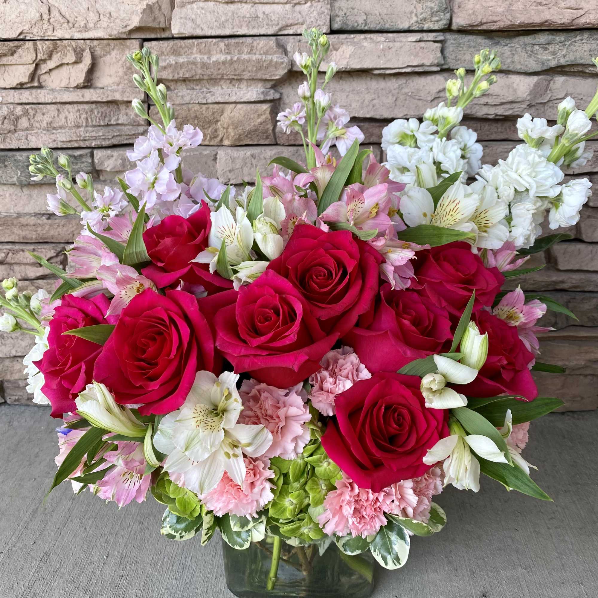 Bouquet of red roses, pink flowers, and white blooms in a glass vase
