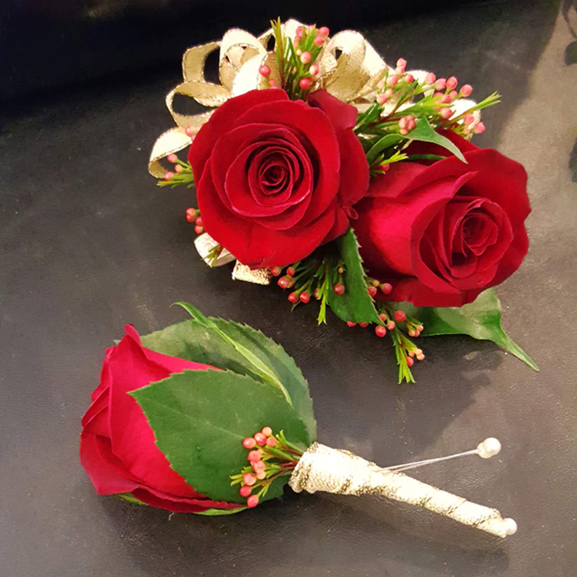 Two red rose boutonnieres with gold ribbon and pearl pins