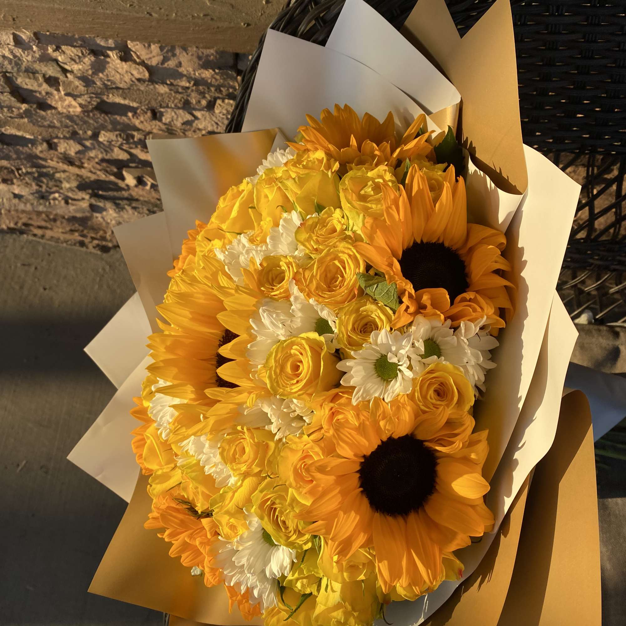 Bouquet of yellow sunflowers, roses, and white daisies wrapped in paper
