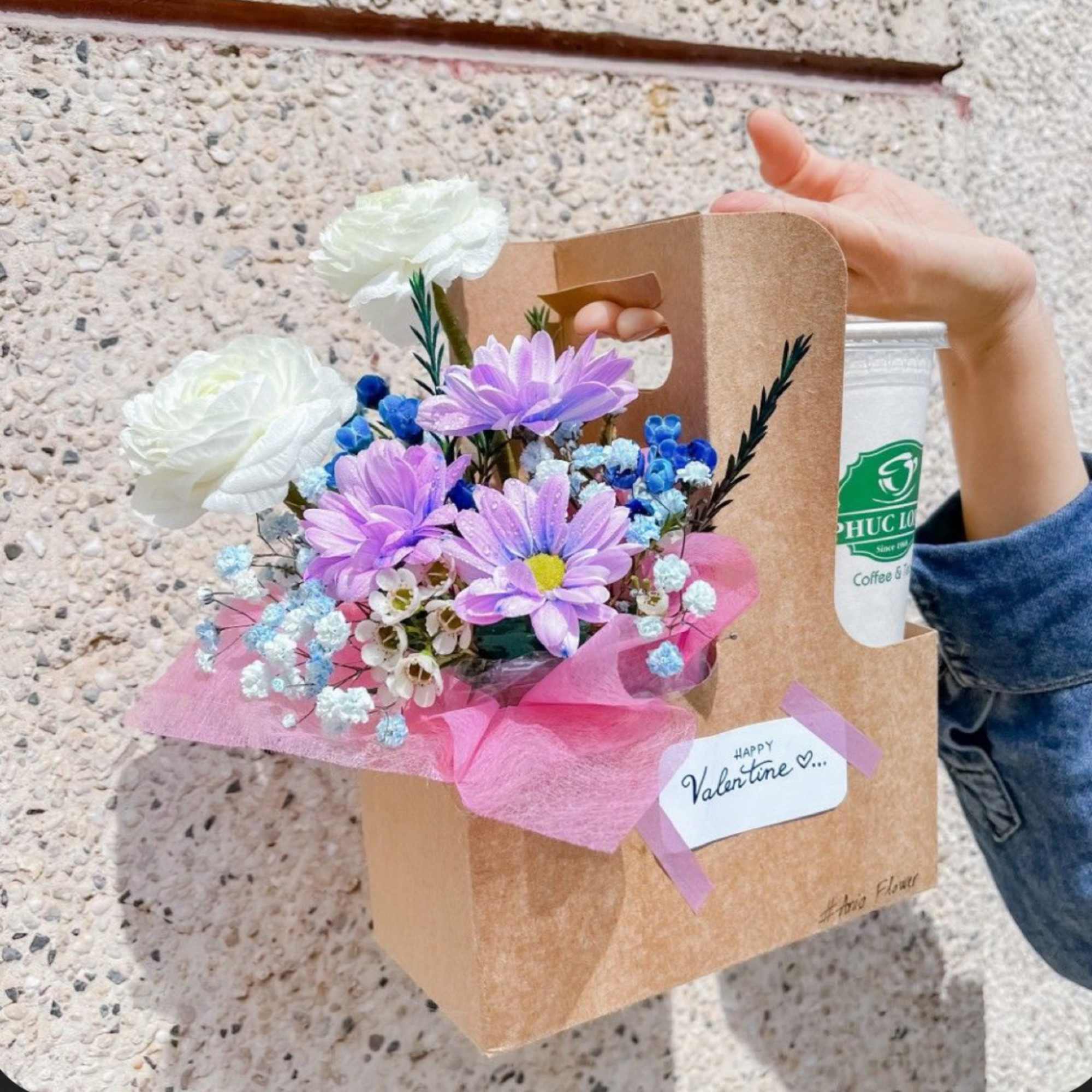 Bouquet of white and purple flowers in a kraft gift bag with a drink cup