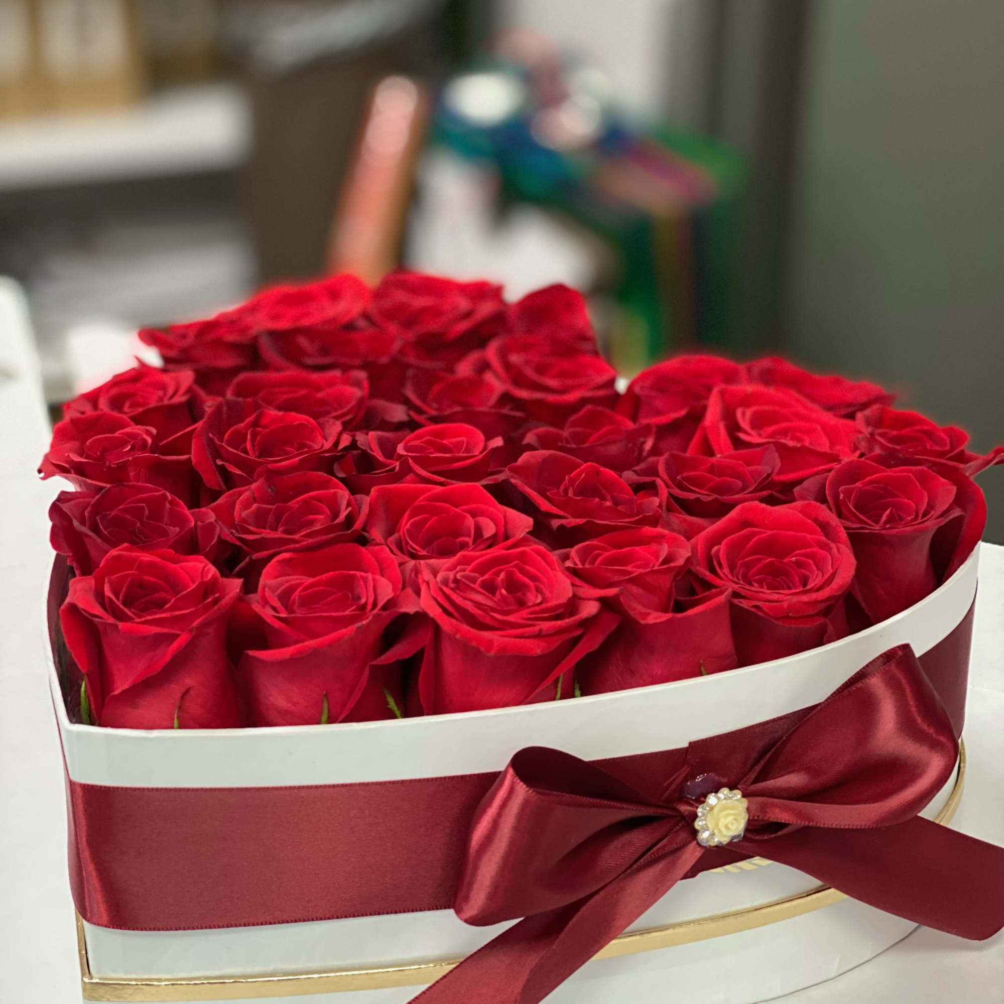 Heart-shaped box filled with red roses and a burgundy ribbon