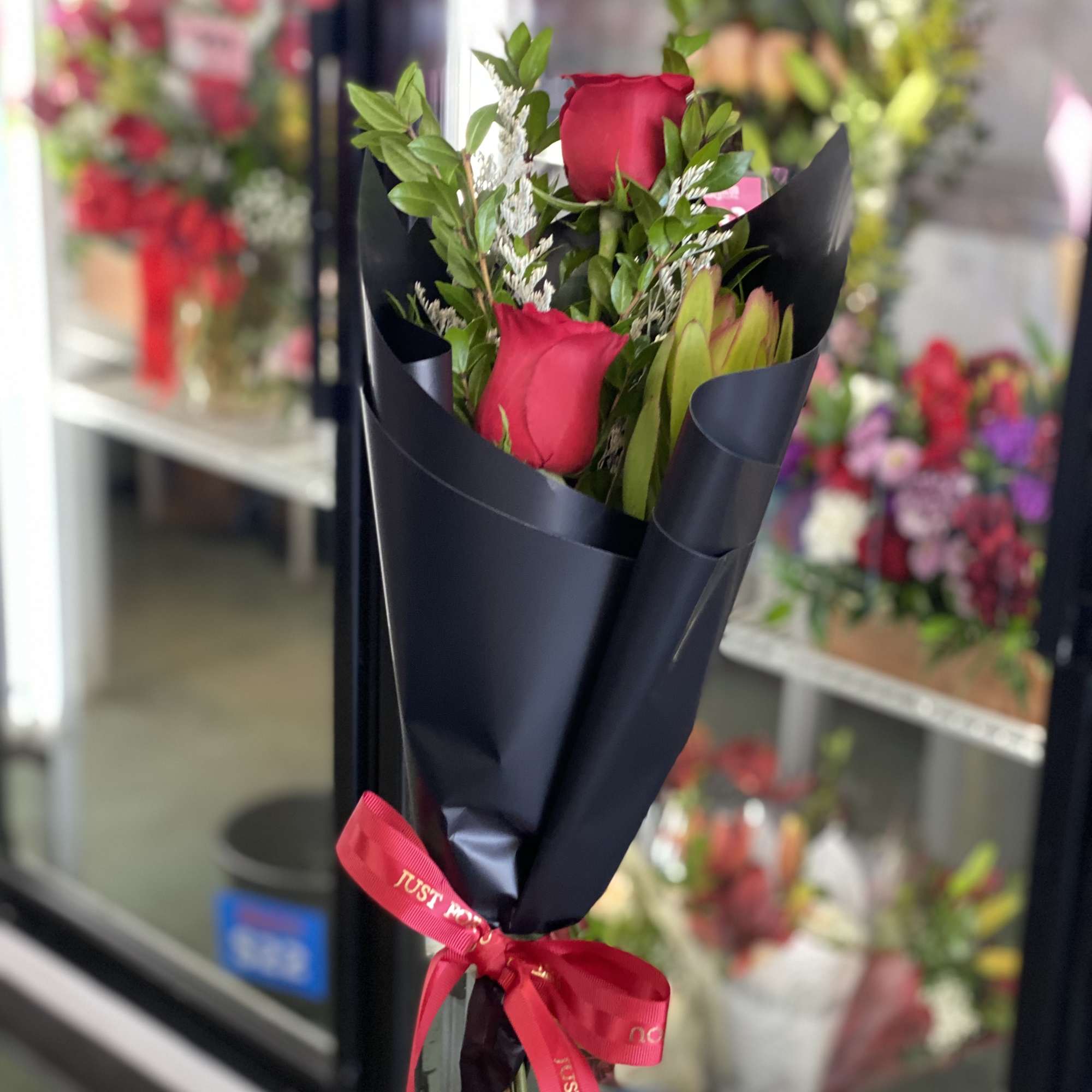 Handheld bouquet of red roses wrapped in black paper with a red ribbon