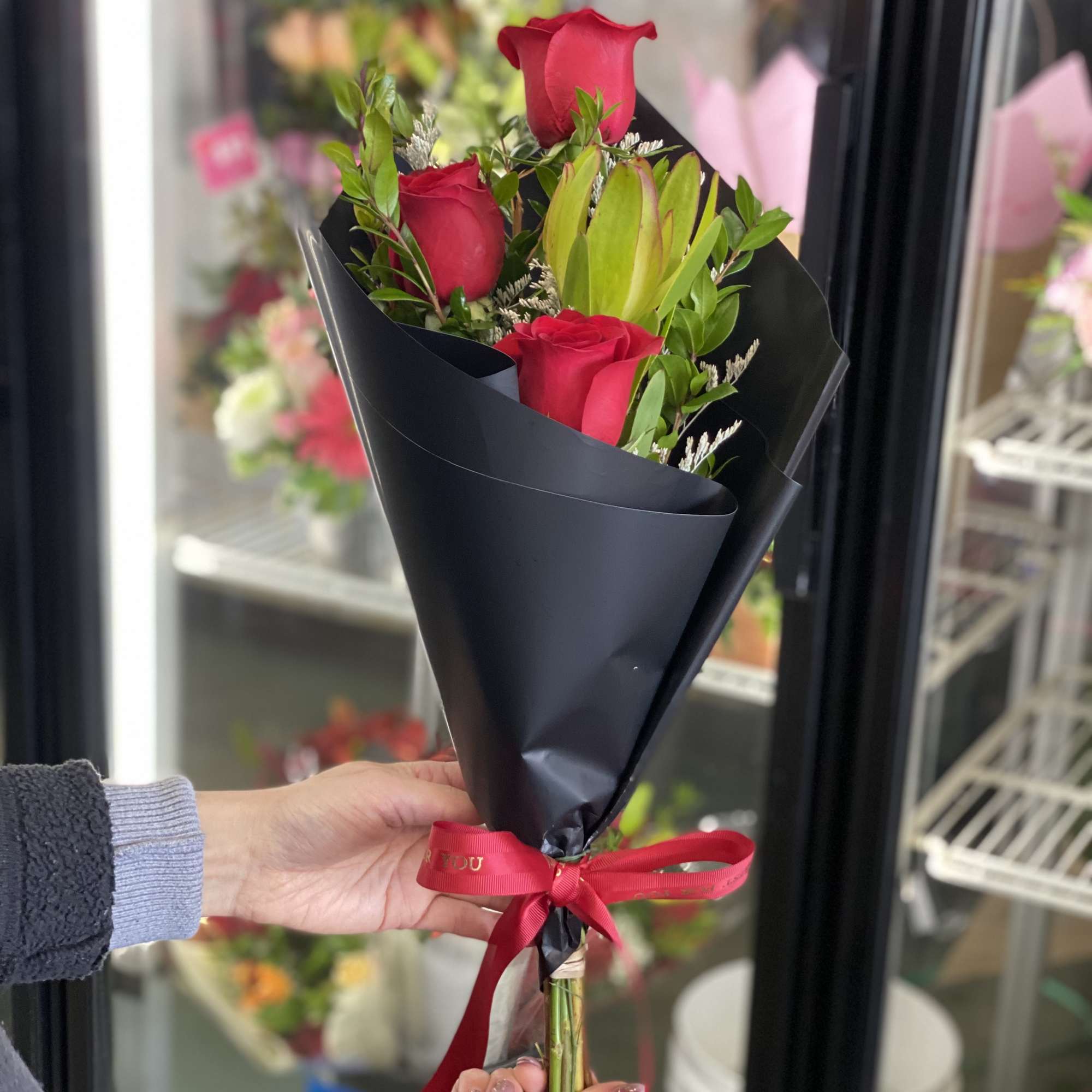 Handheld bouquet of red roses wrapped in black paper with a red ribbon