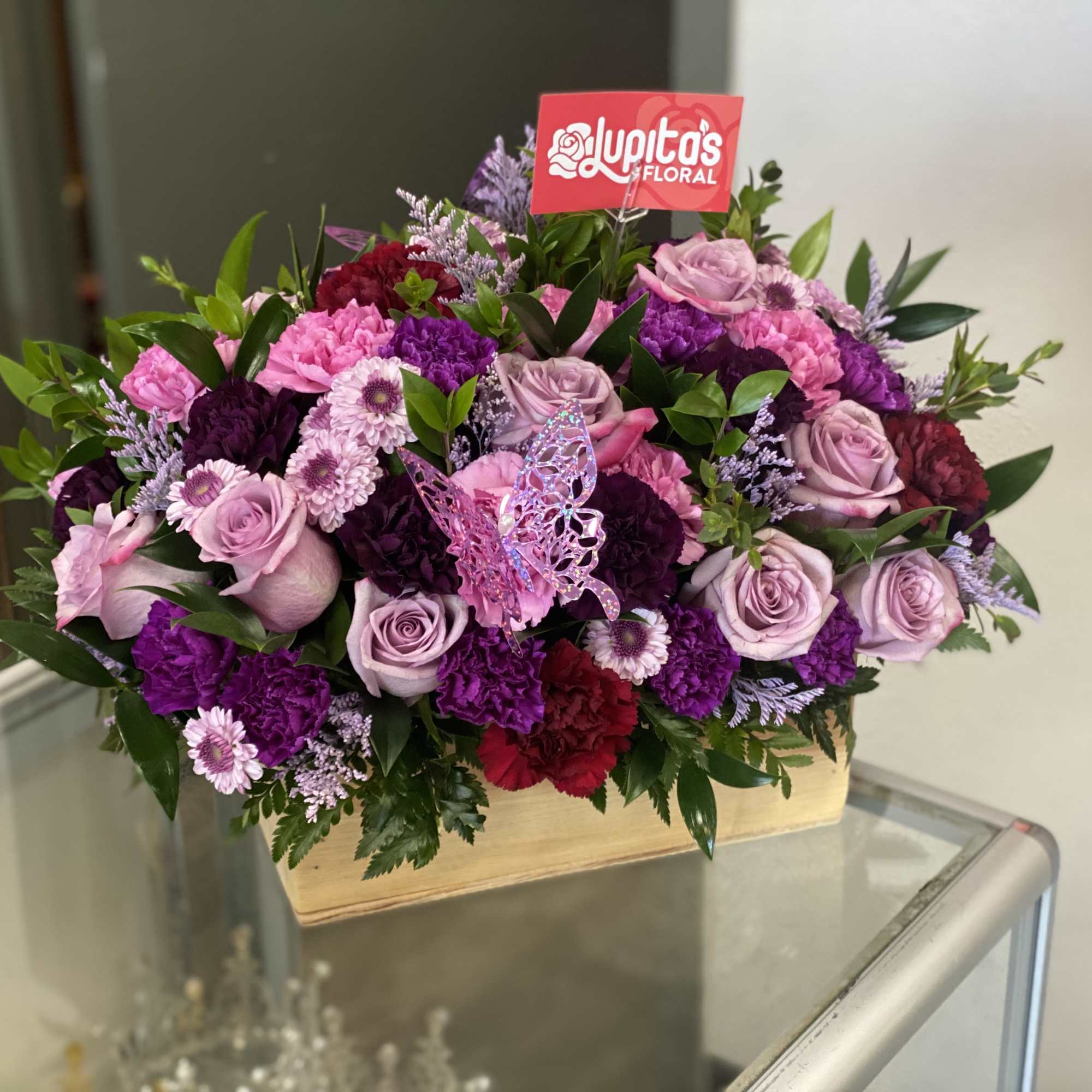 Pink and purple floral arrangement in a wooden box with a butterfly pick