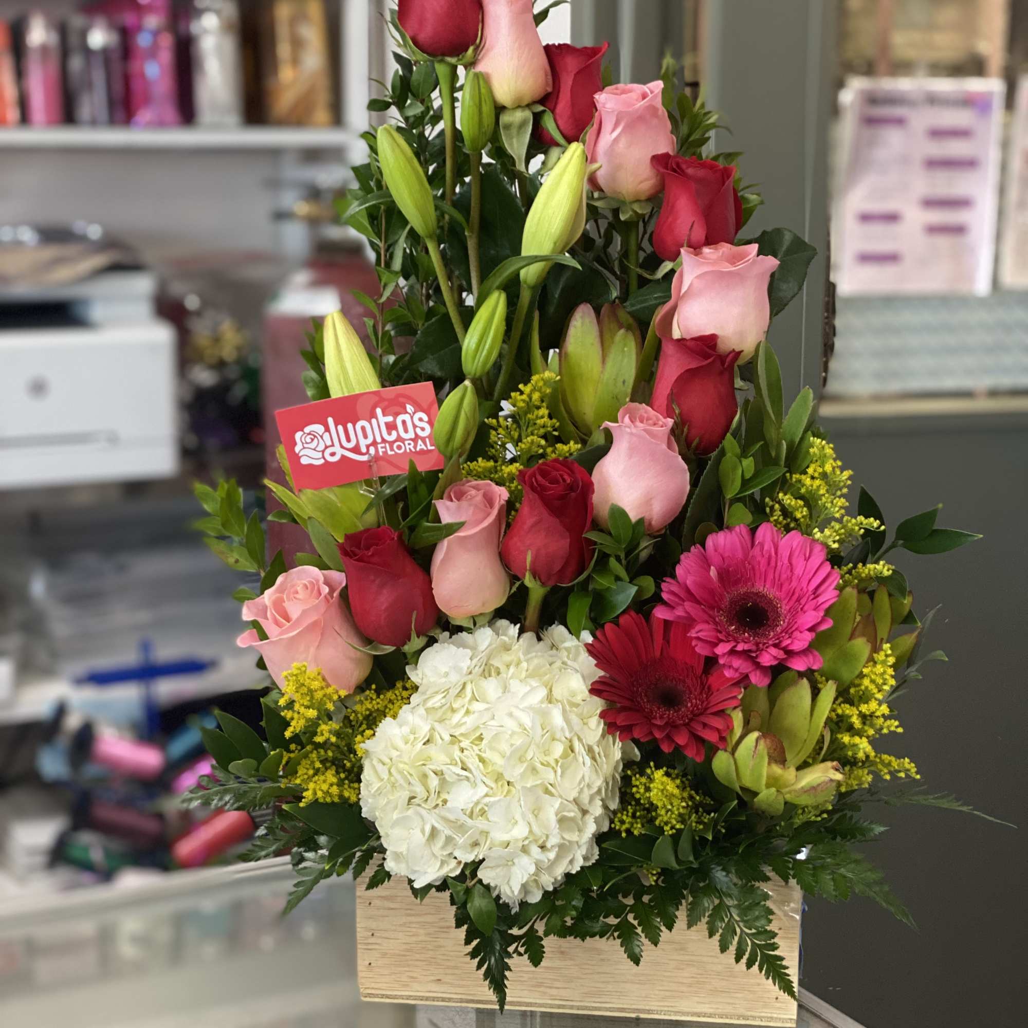 Tiered bouquet of pink and red roses with white hydrangea in a wooden box
