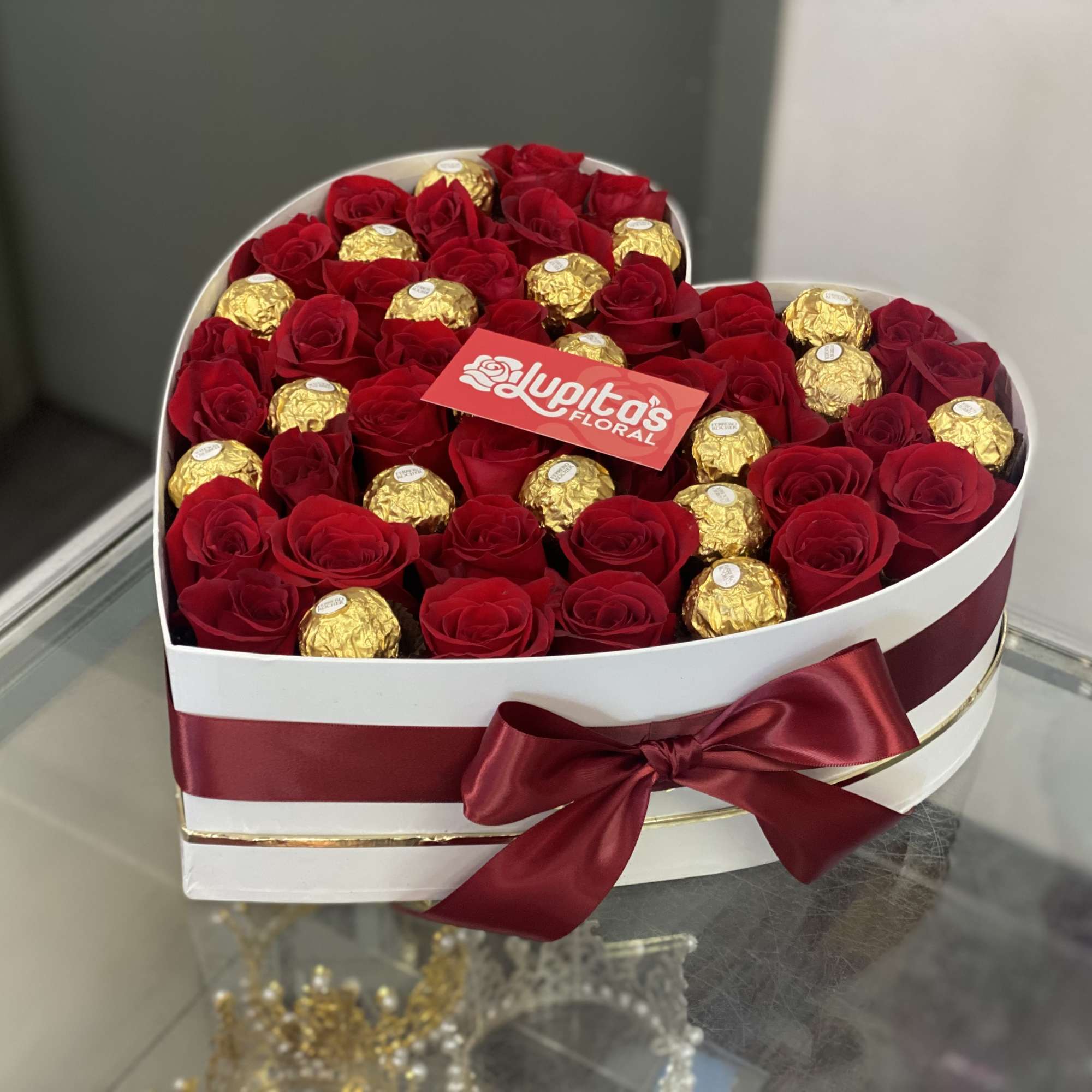 Heart-shaped box of red roses with gold-wrapped chocolates and a burgundy ribbon