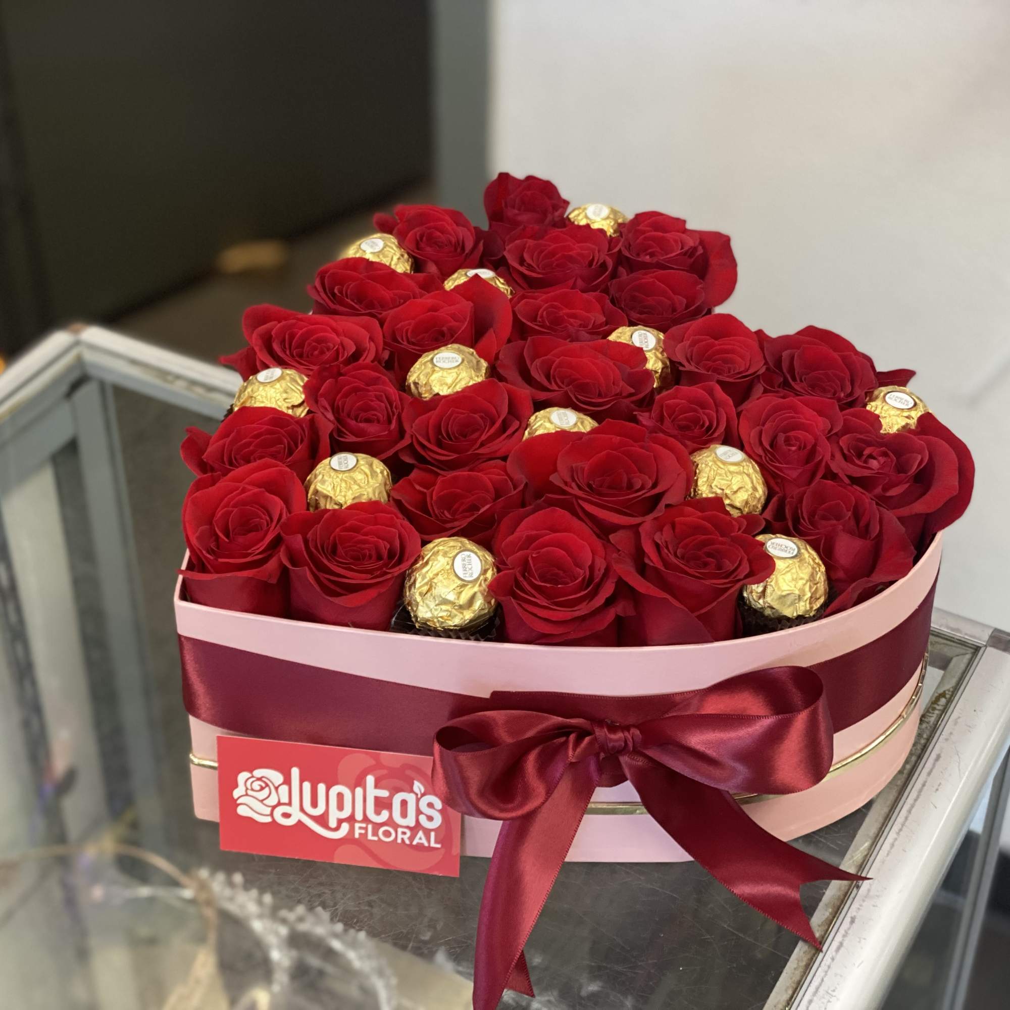 Round box of red roses with gold-wrapped chocolates and a burgundy ribbon