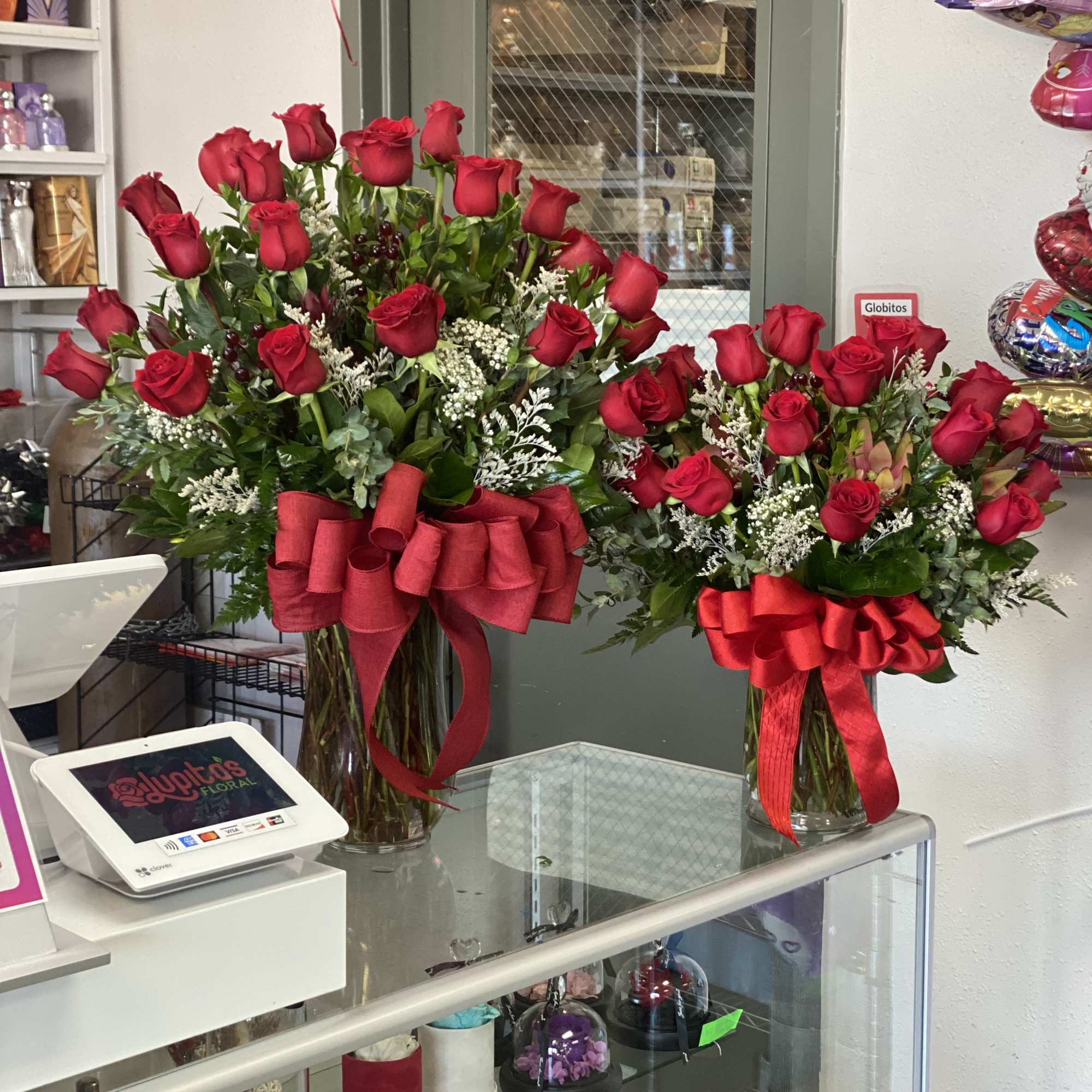 Two tall bouquets of red roses in glass vases with red bows