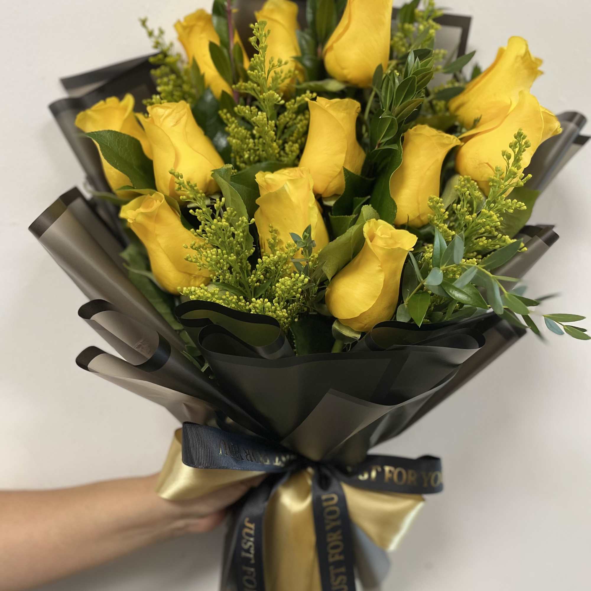 Bouquet of yellow roses wrapped in black paper with a gold ribbon